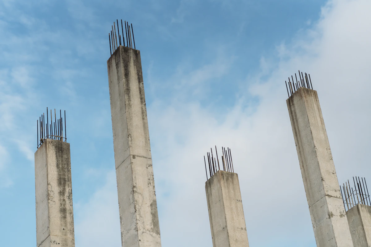 Pilares de betão armado com armadura de aço contra o céu, representando a estrutura de uma casa
