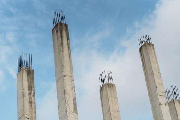 Pilares de betão armado com armadura de aço contra o céu, representando a estrutura de uma casa