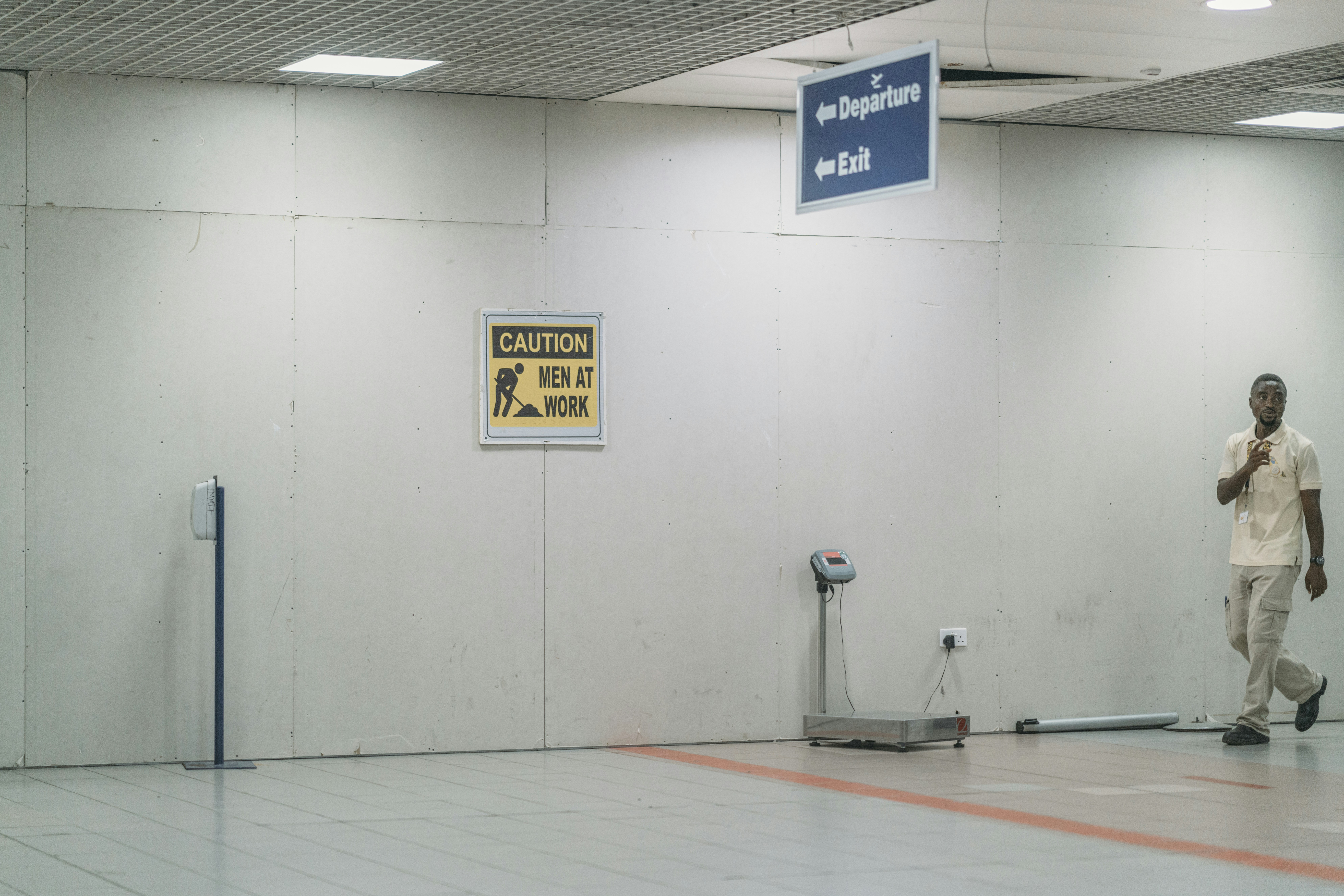 Airport worker walks past caution sign and departure exit.