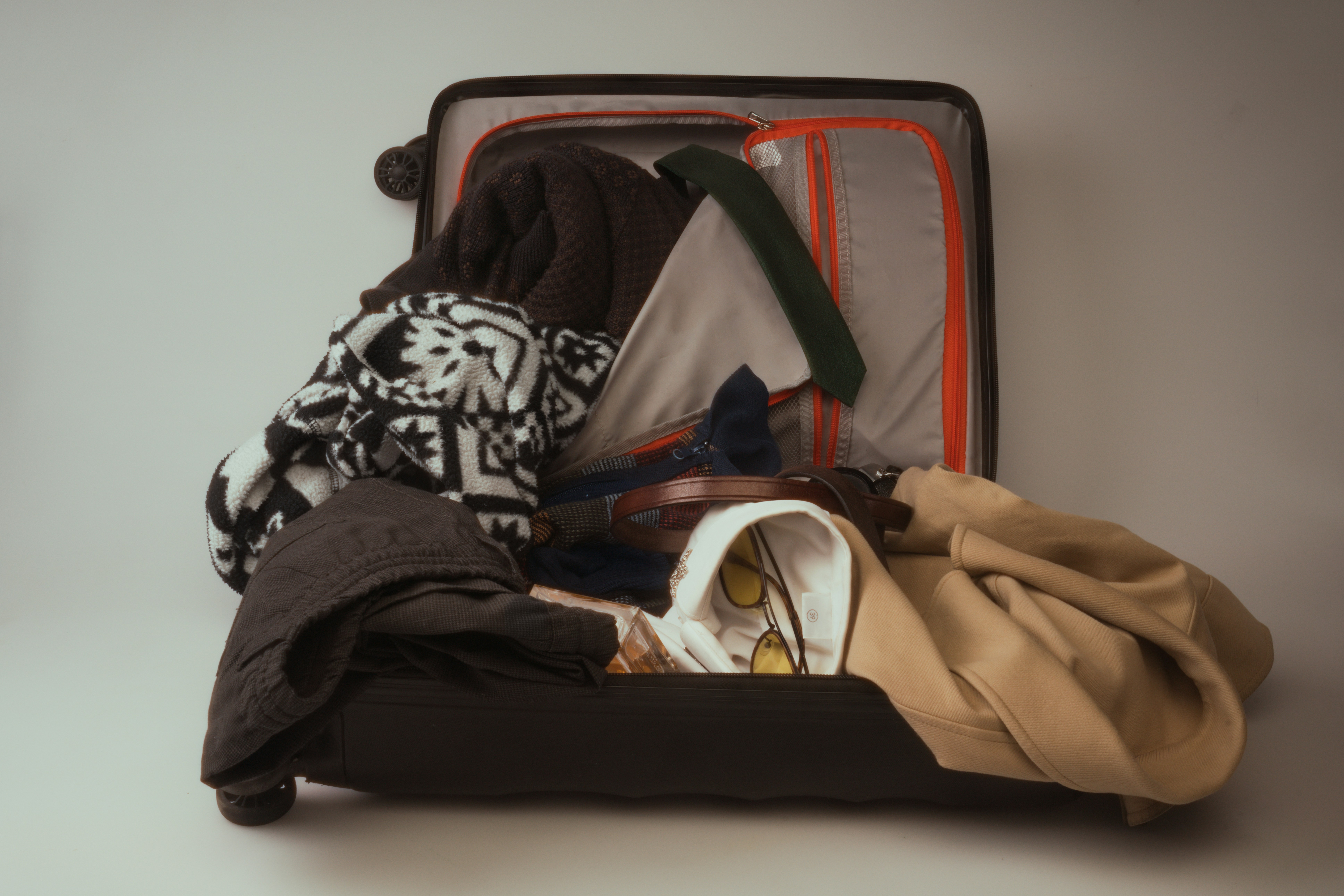 An open suitcase overflowing with various clothes.