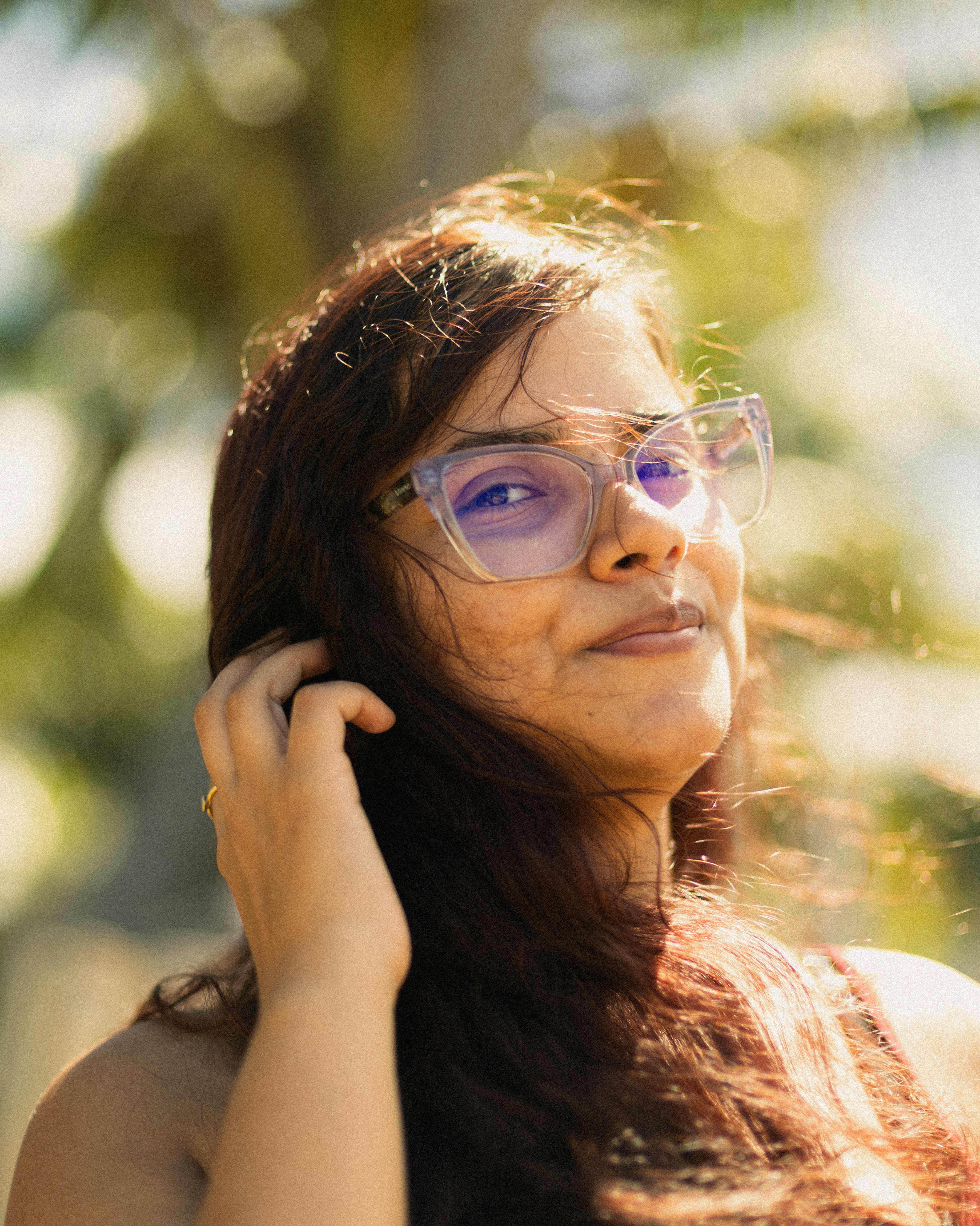 Una giovane donna con gli occhiali sorride all'aperto al sole.