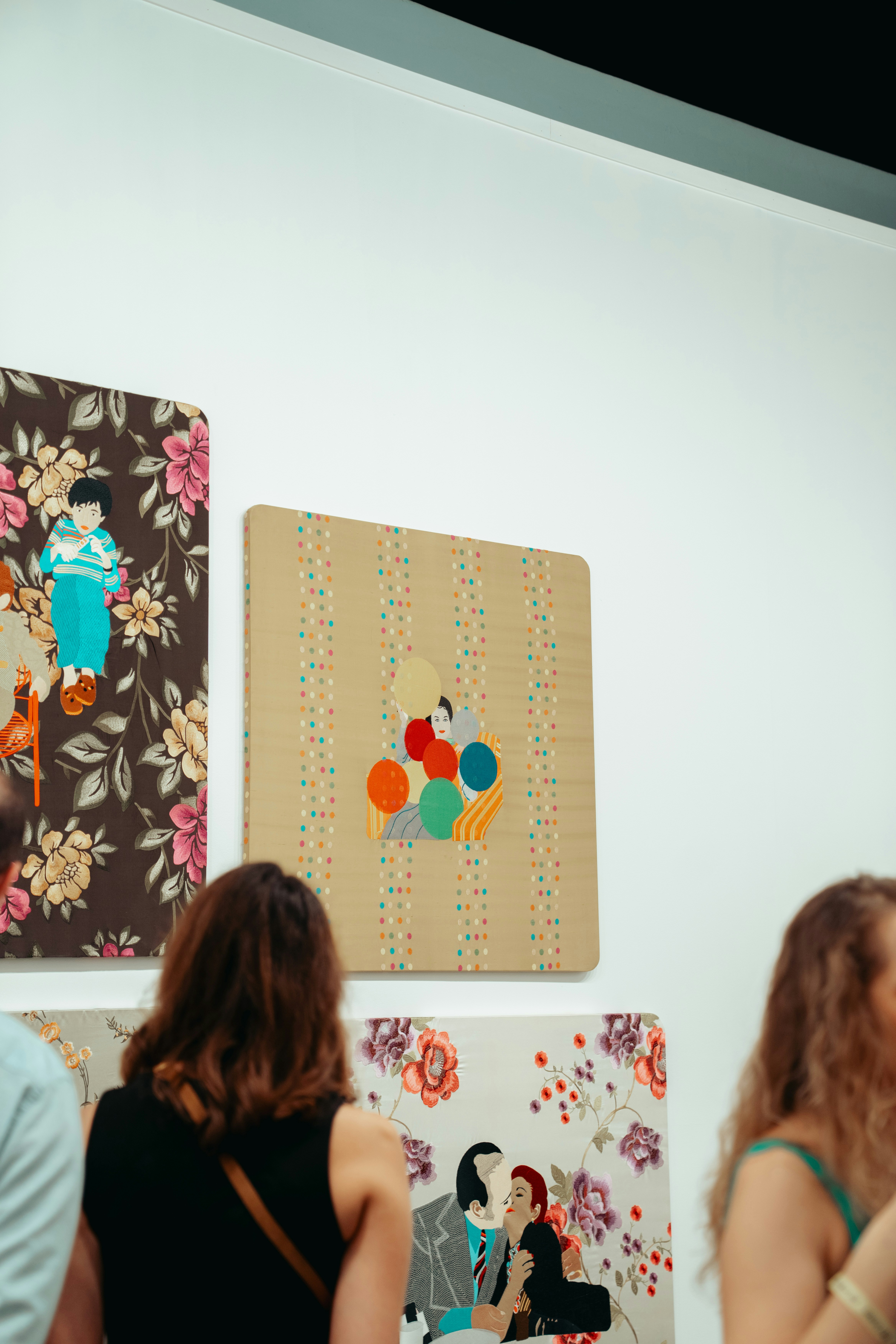 Pessoas assistindo a obras de arte coloridas em uma parede branca de galeria.