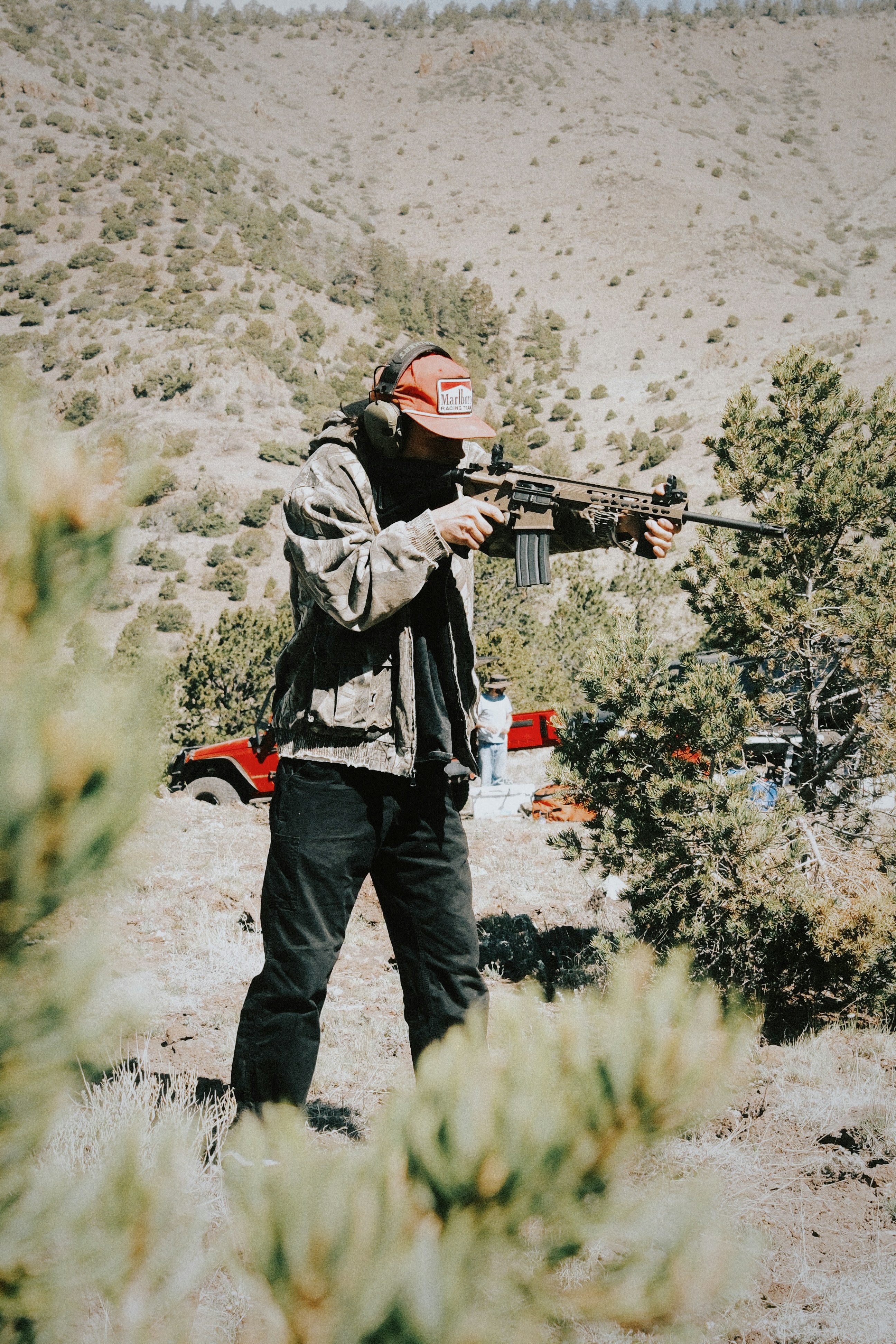 Un homme tirant au fusil dans un paysage sec et vallonné.