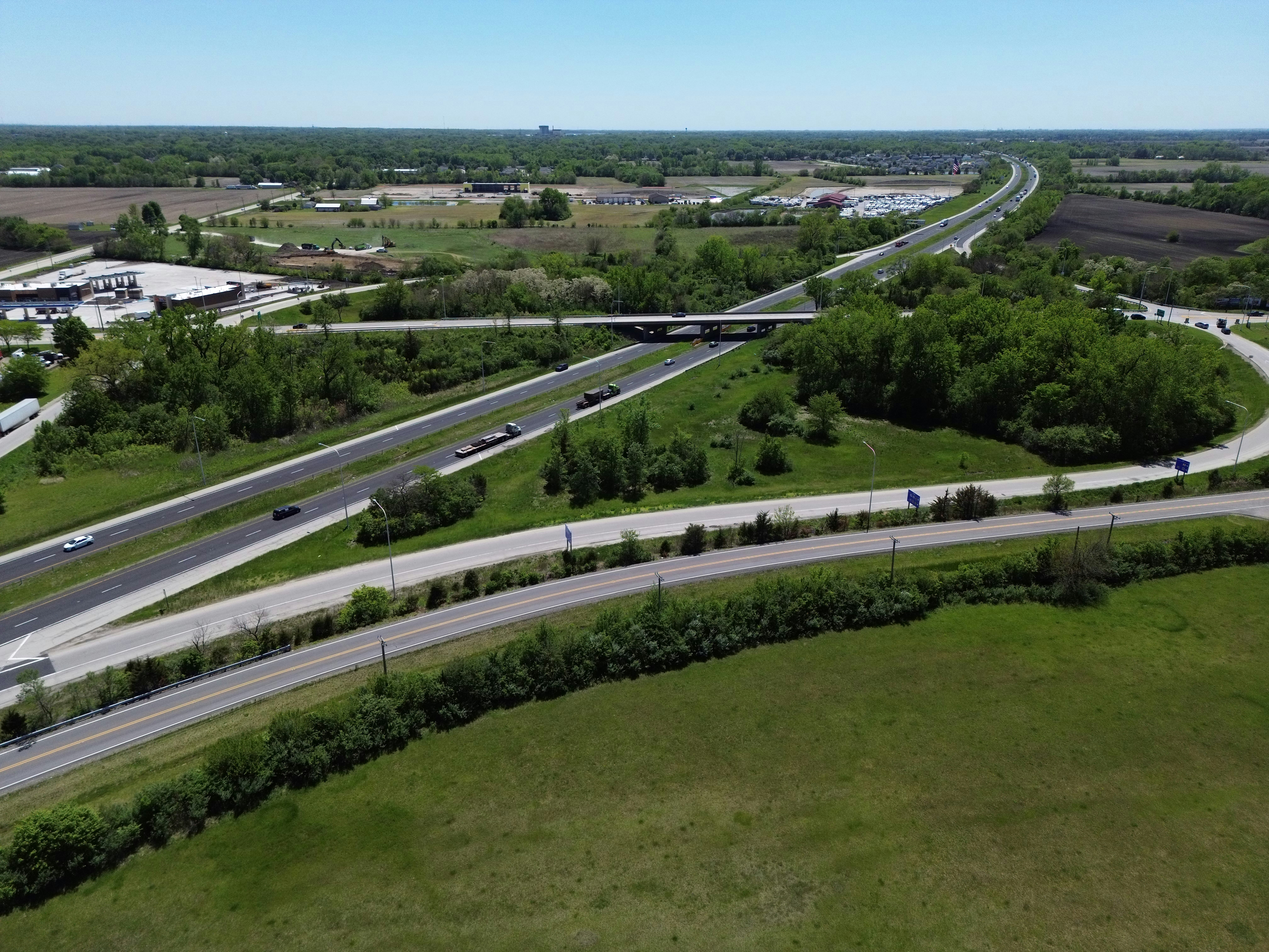Highway interchange with multiple roads, green fields, and trees.
