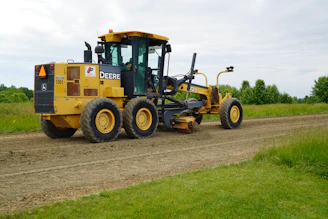 Yellow john deere road grader on a gravel road.