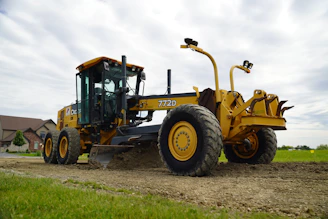 A large yellow road grader on a dirt path.
