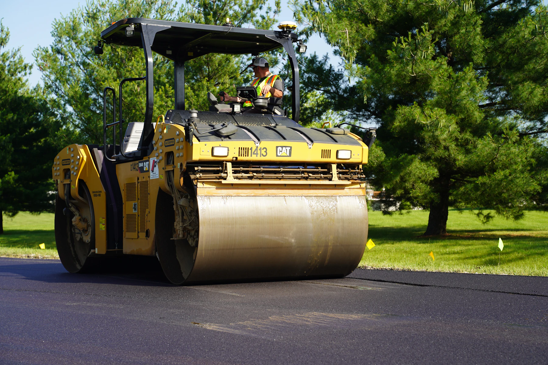Yellow road roller compacting fresh black asphalt outdoors