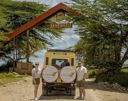 Two people with a safari vehicle under a serengeti archway