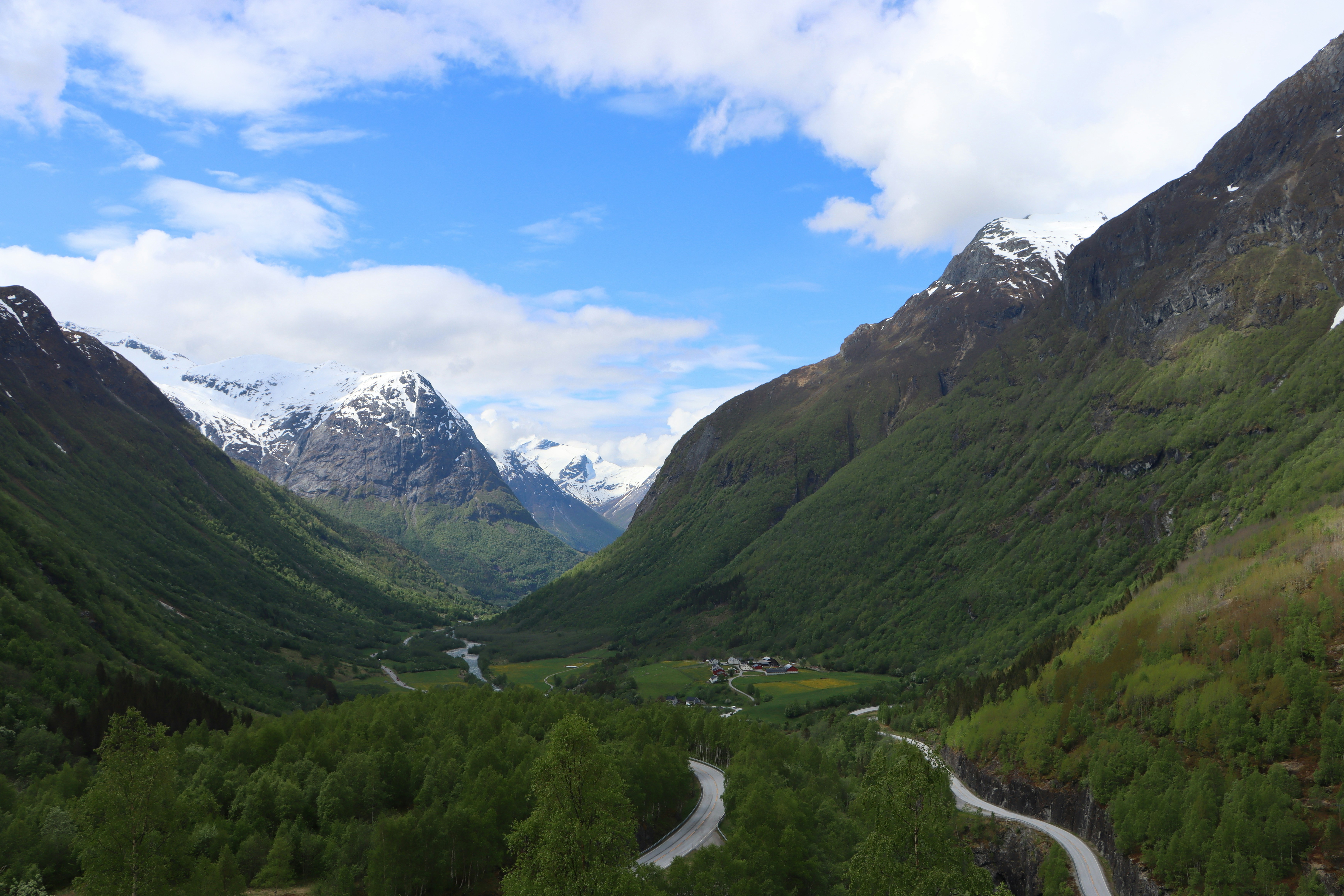 Winding roads through a green valley with snow-capped mountains.