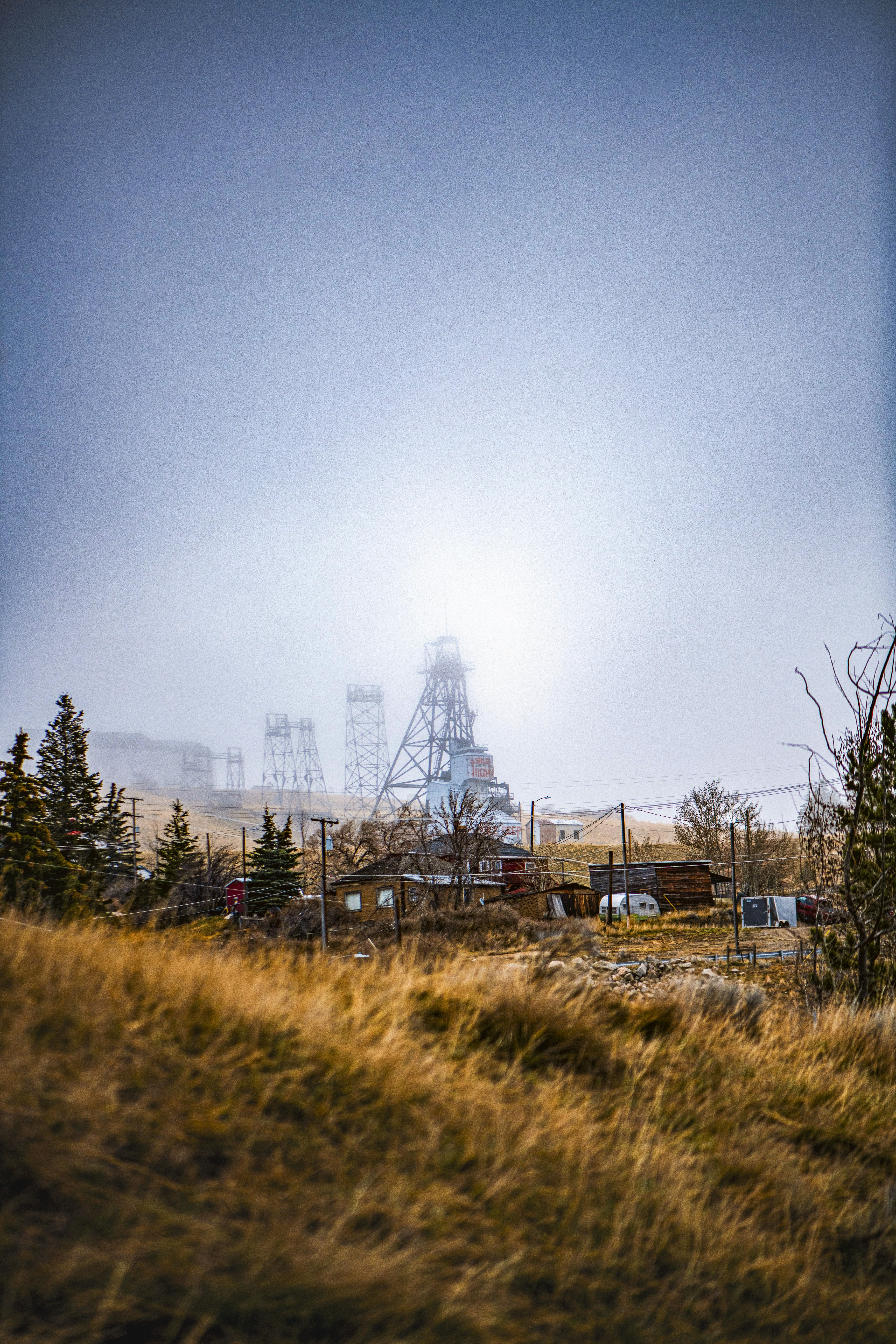 흐릿한 하늘과 마른 풀 아래 헤드프레임이 있는 채굴 시설.