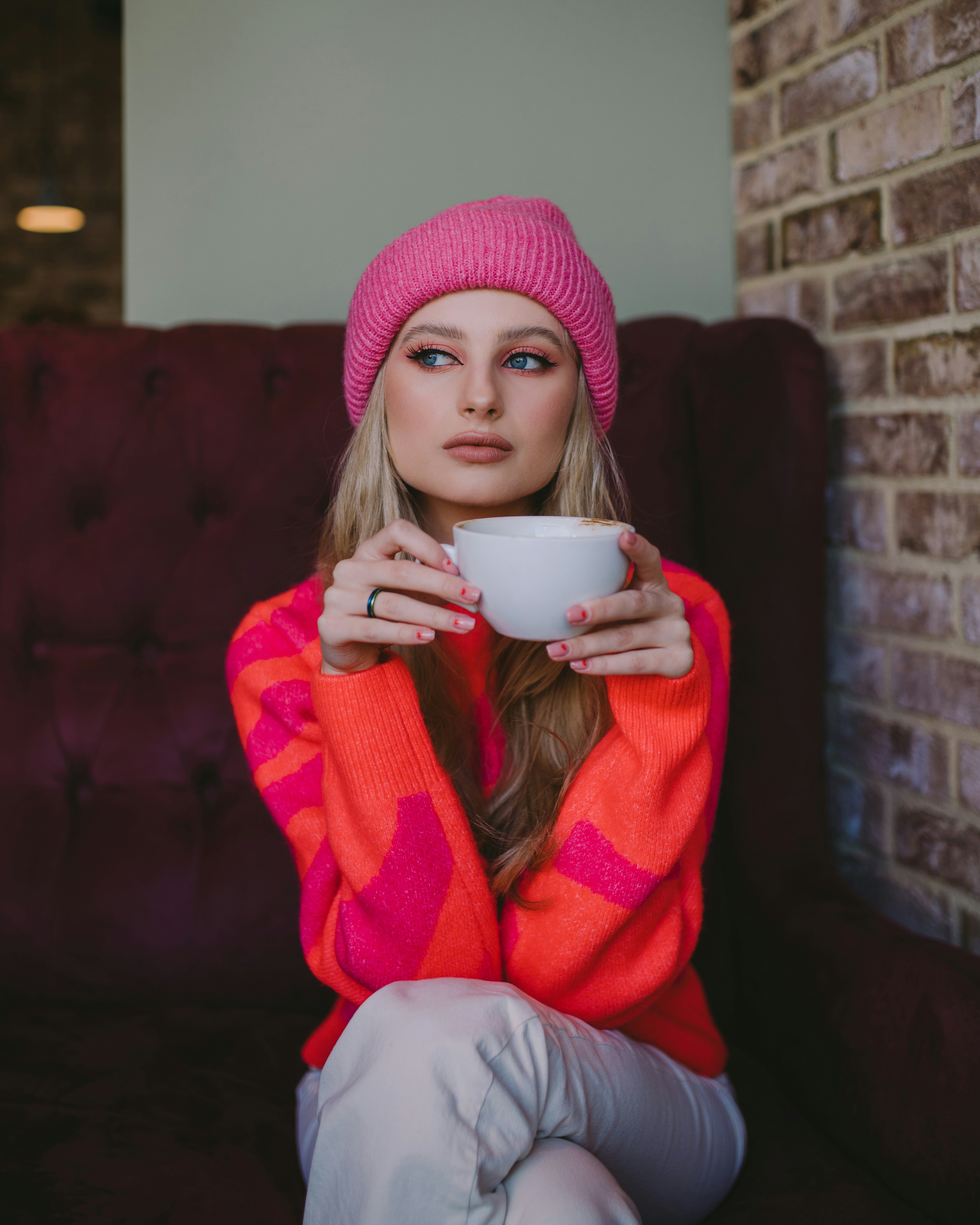 Woman in pink beanie holds coffee cup in cafe.