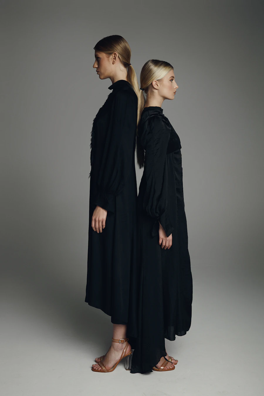 Two models in long black dresses standing back to back