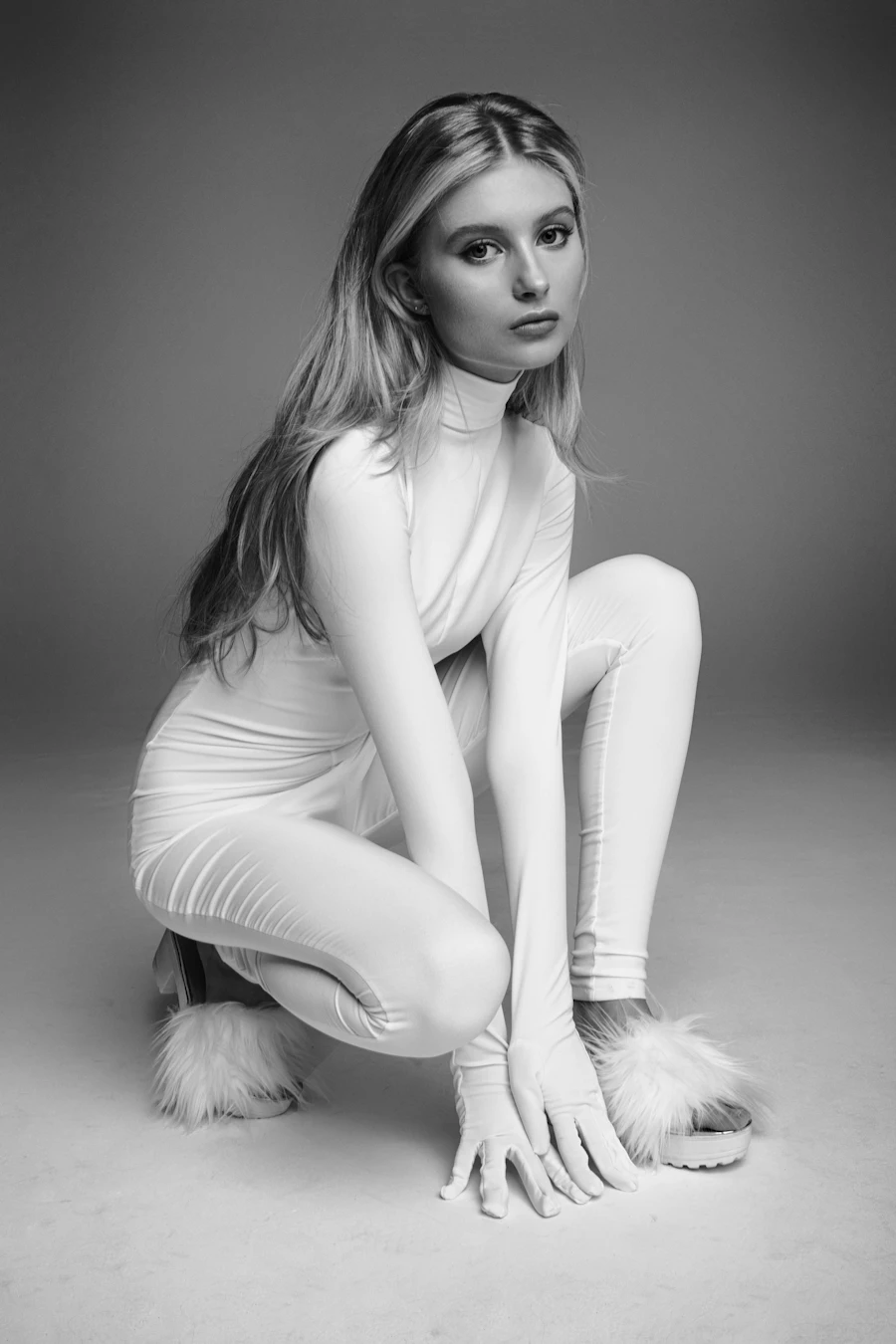Model in a white outfit crouching in the studio