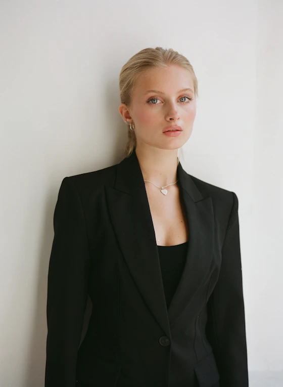 Young woman in black blazer standing against a white wall