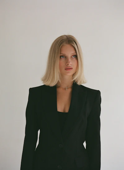 A young blonde woman in a black blazer looking away.