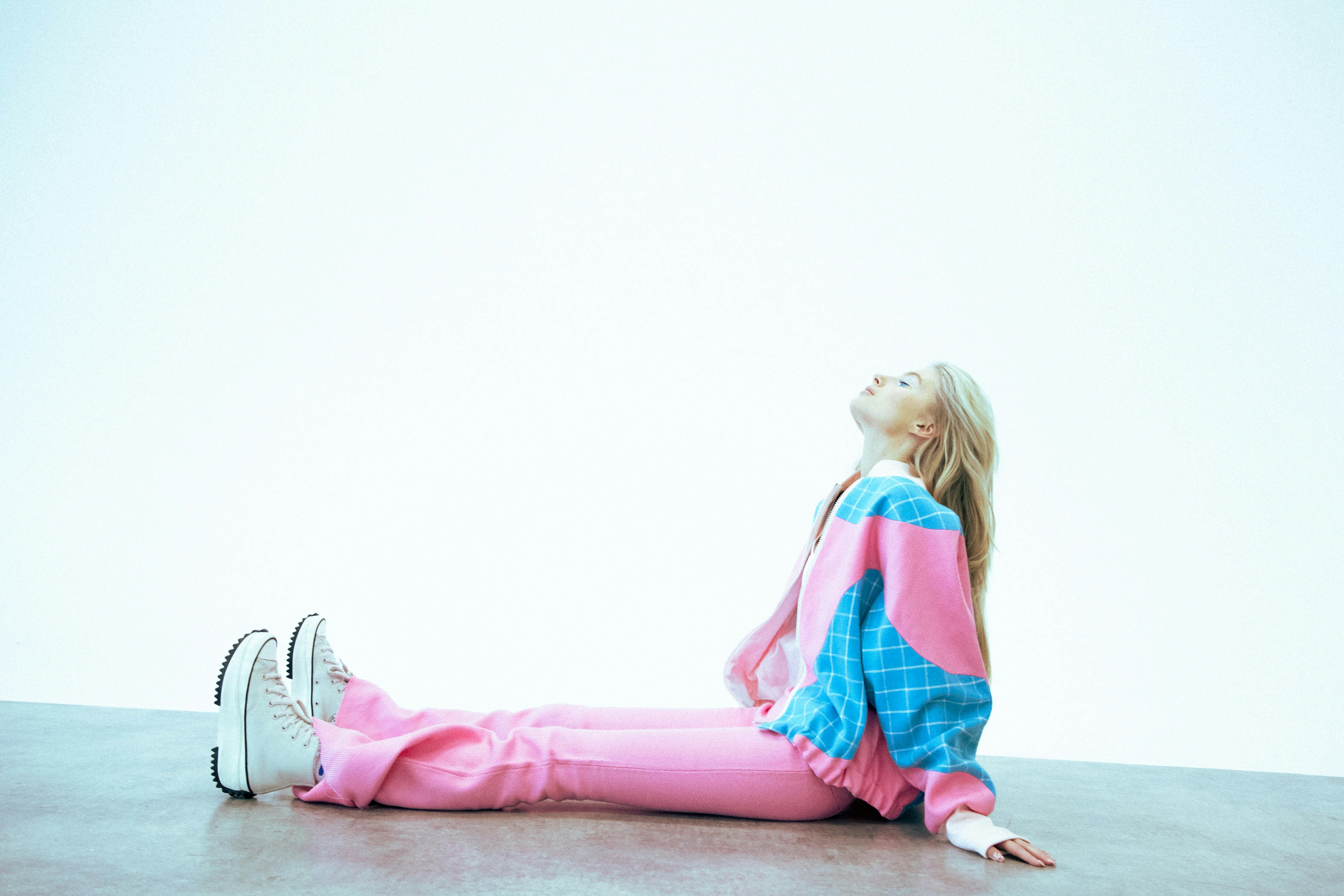 Young person in colorful tracksuit sitting on floor, looking up.