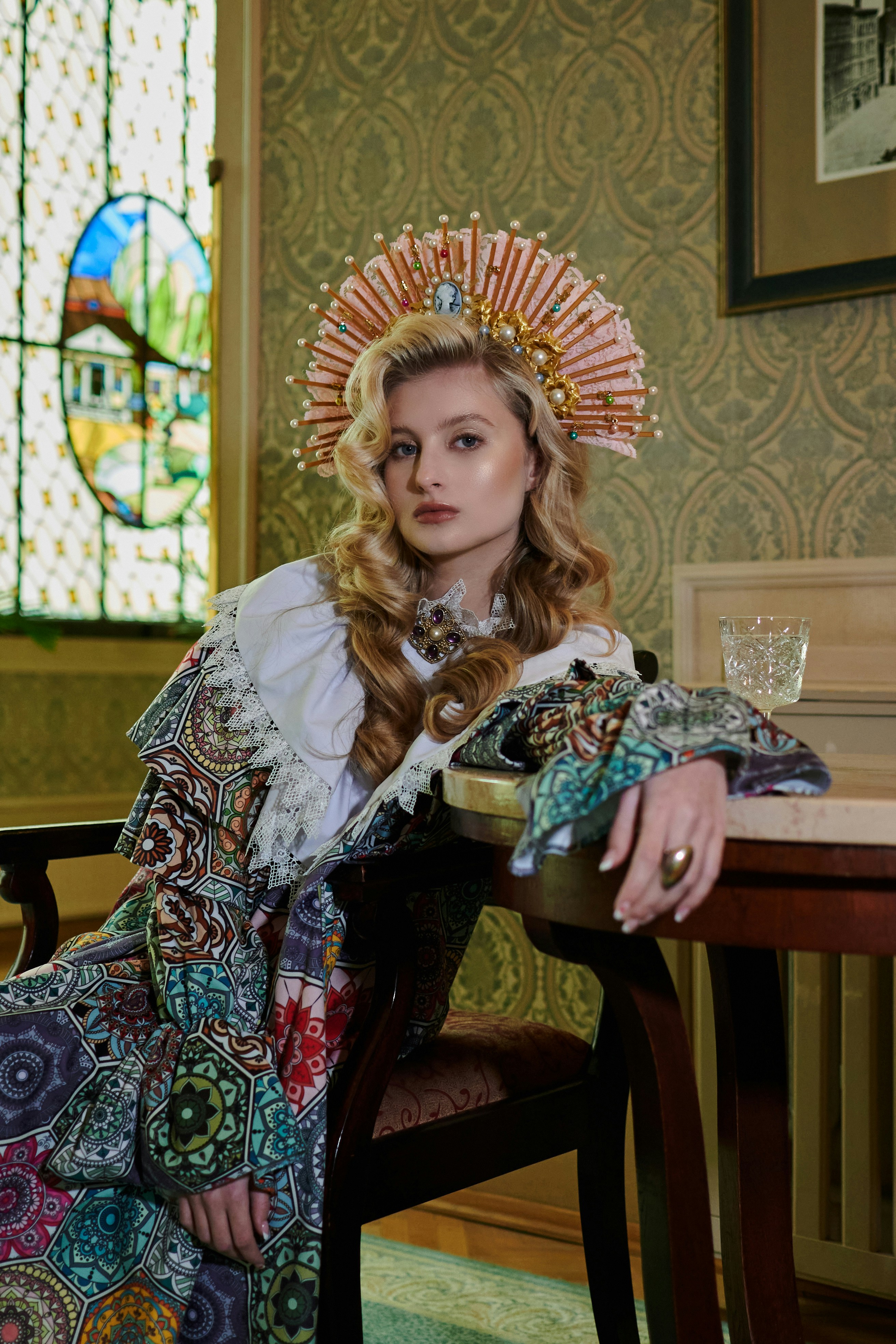 Una mujer elegante con coloridos atuendos tradicionales se sienta en una mesa.