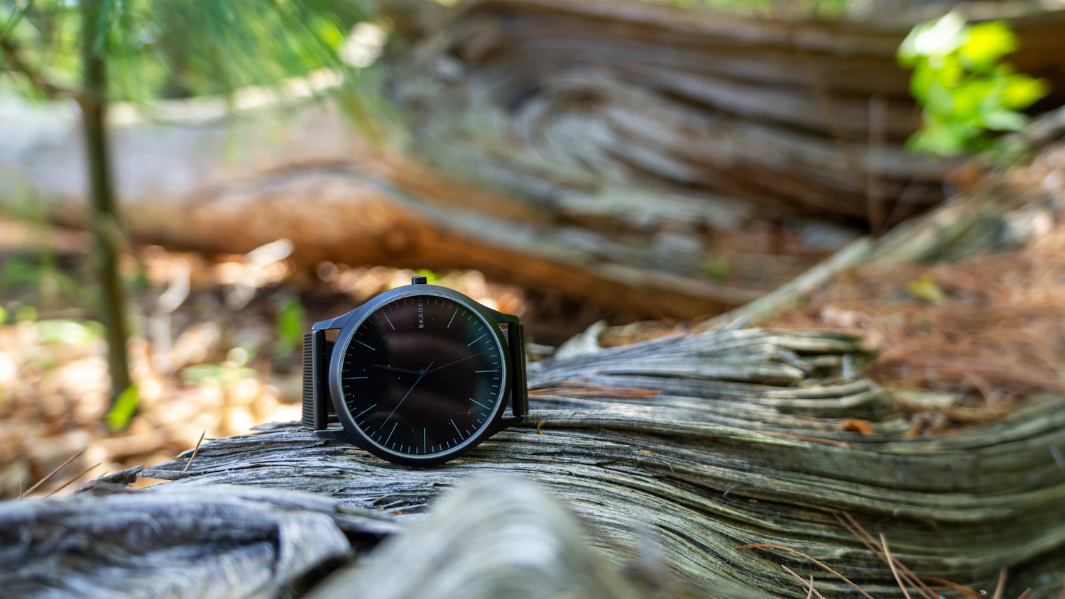 Jura 40 Nuit, an all-black watch on a black mesh bracelet resting on a weathered log