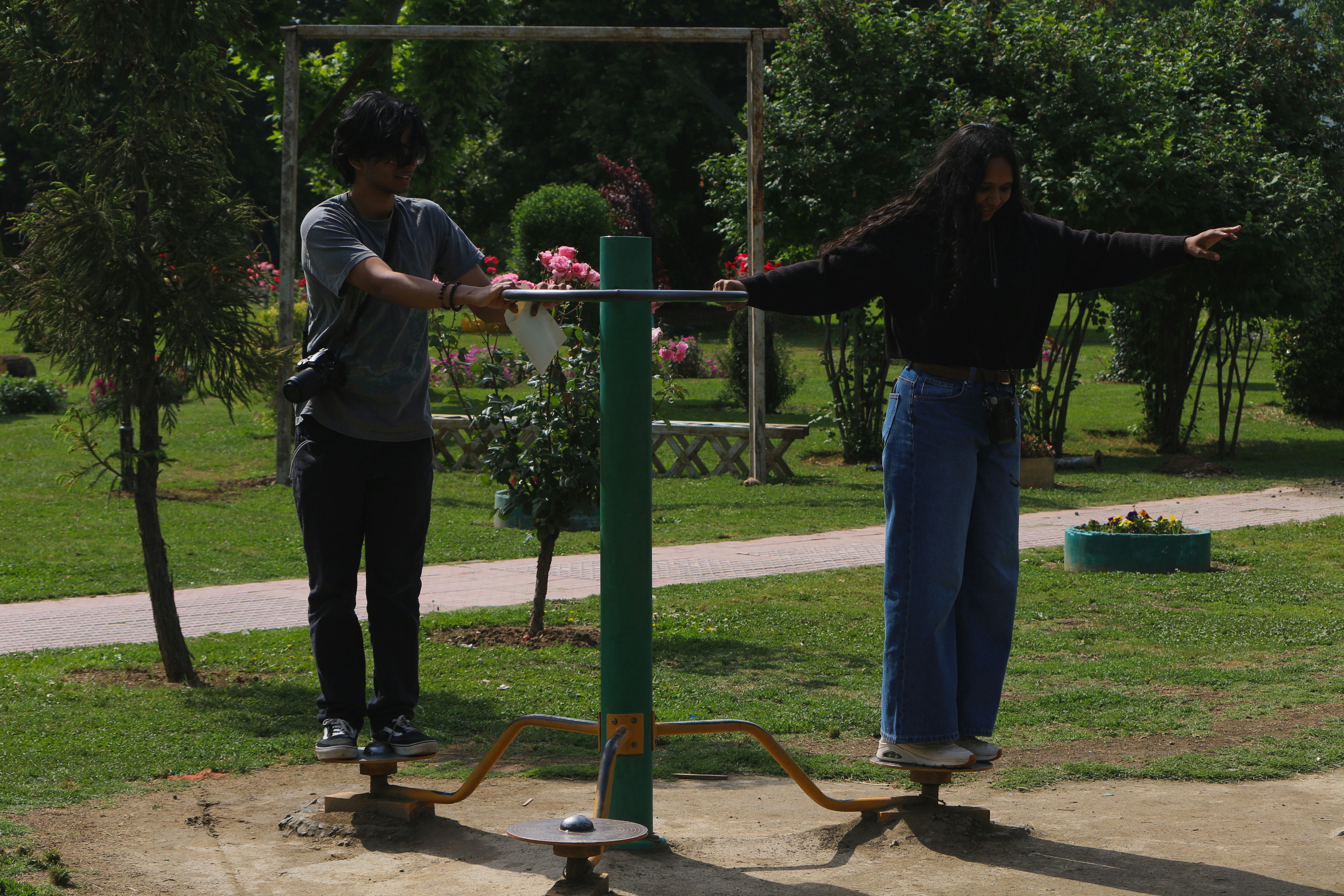 Two people balancing on outdoor exercise equipment in a park.
