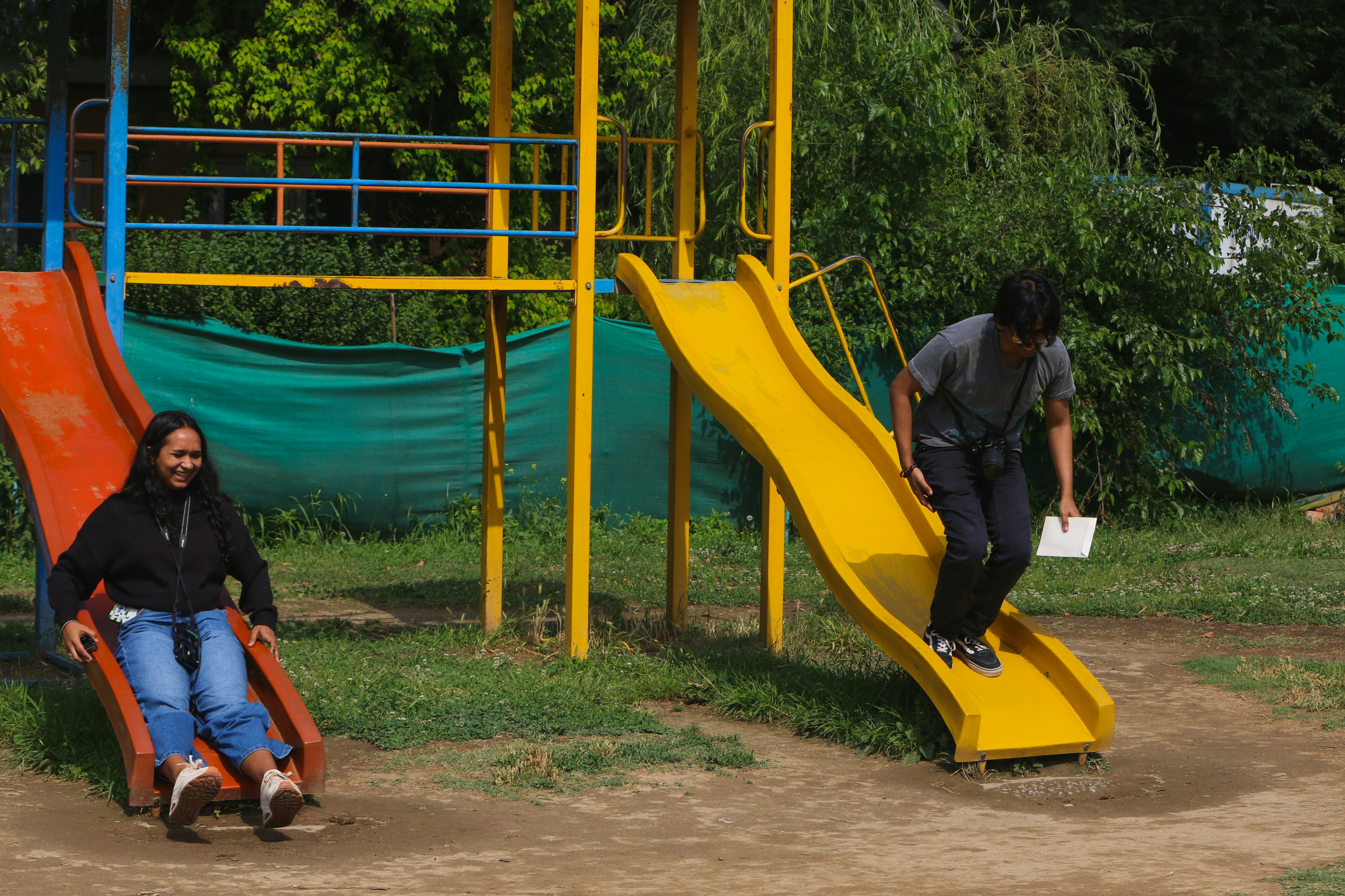 Two people enjoying slides in a sunny playground.