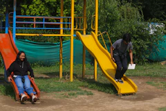 Two people enjoying slides in a sunny playground.