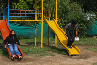 Two people enjoying slides in a sunny playground.