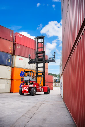 A red reach stacker moving containers in a shipping yard.