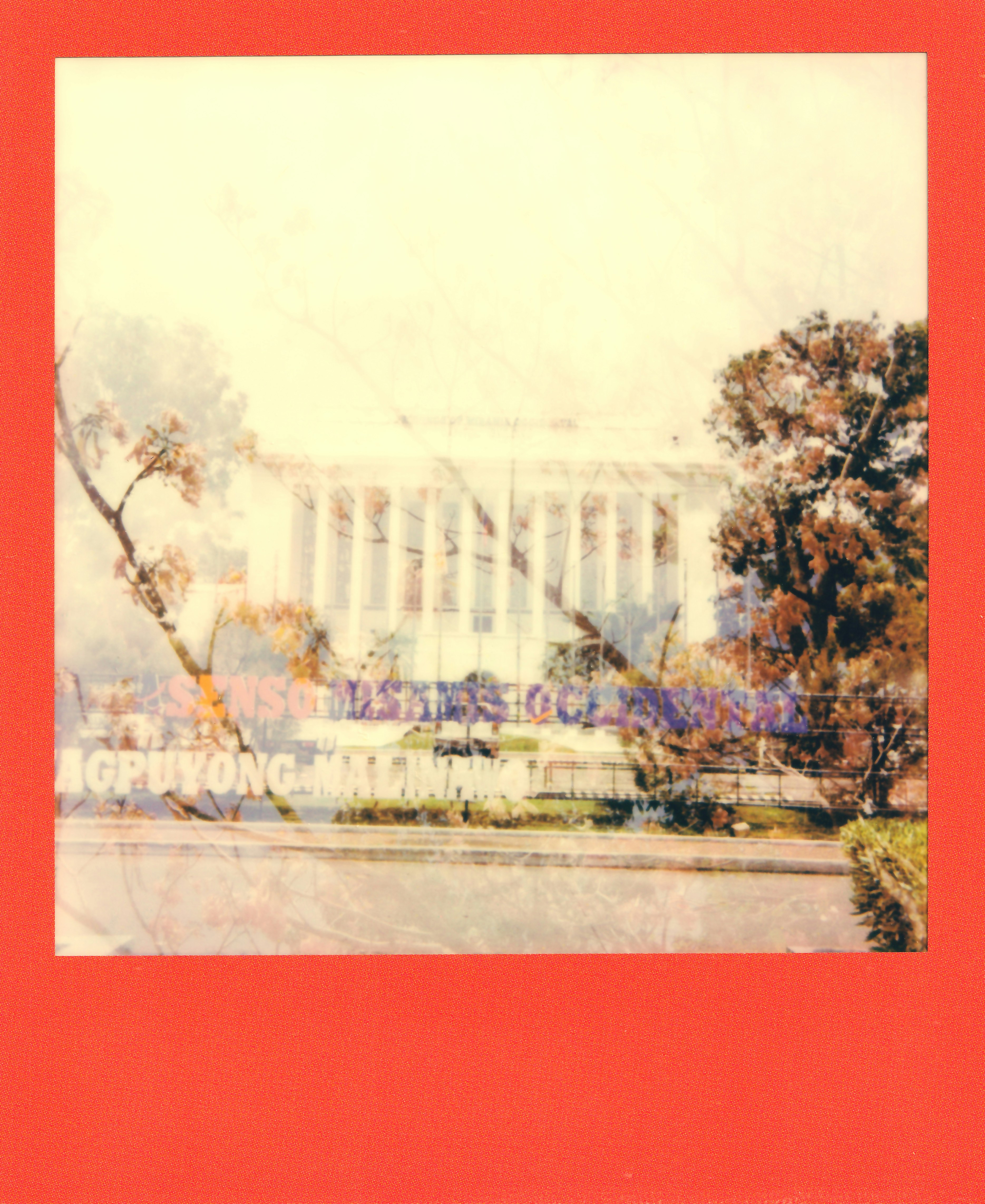 Faded view of a large building with columns and trees.