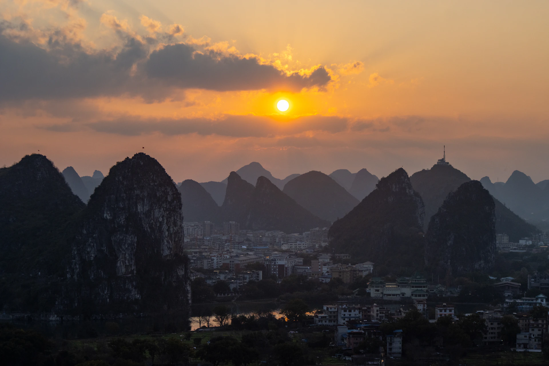 Sunset over a city surrounded by numerous karst mountains.