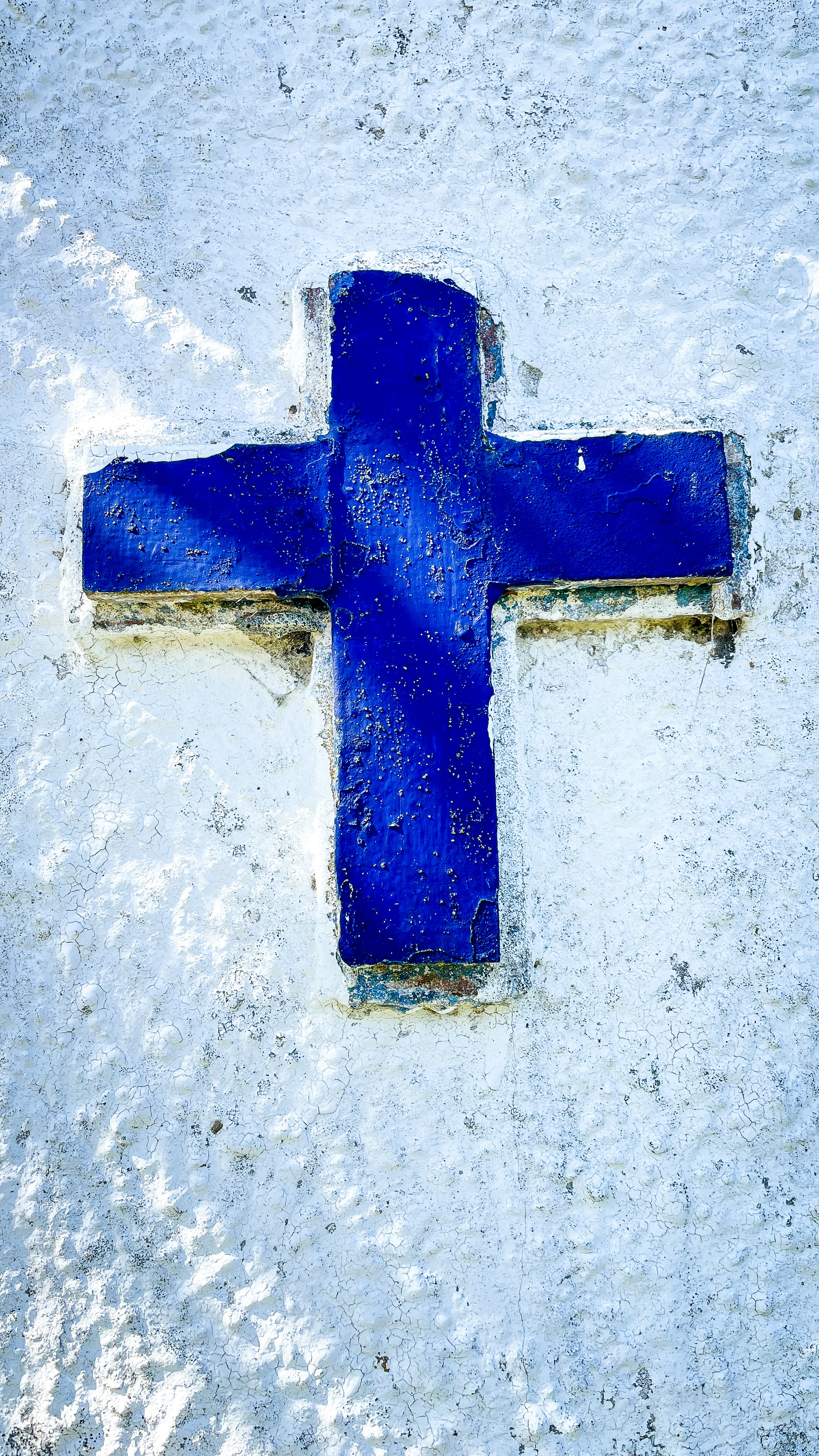 Sunlit blue cross on a weathered white stucco wall.