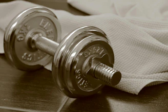 Chrome dumbbell and towel on dark wood.