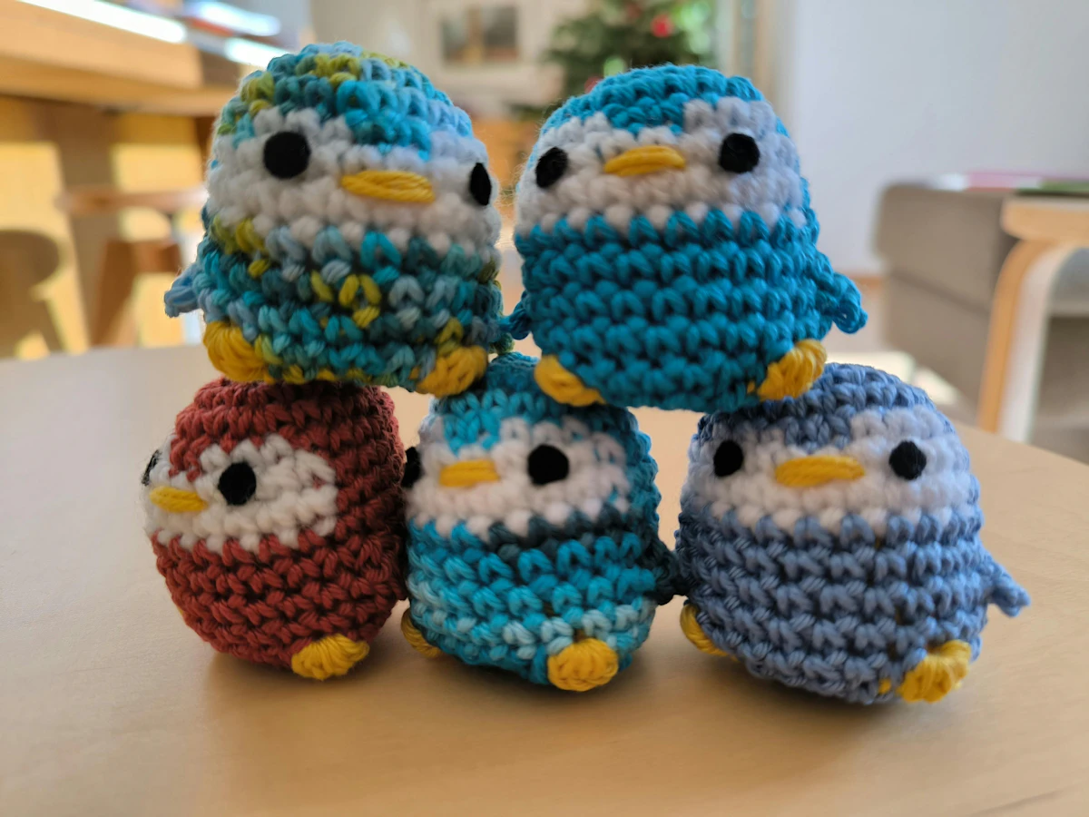Pinguins de amigurumi em crochê enfileirados sobre fundo neutro