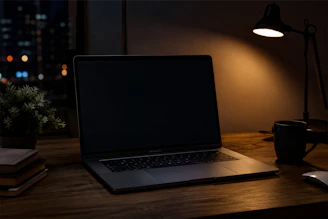 Closed laptop on a dark desk beside a warm lamp, can't stop thinking about work at night