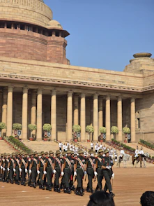 Soldiers marching in formation past a grand classical building.