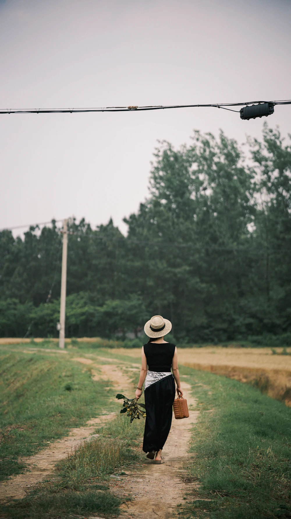 A woman in a sun hat walking along a quiet country track, seen from behind