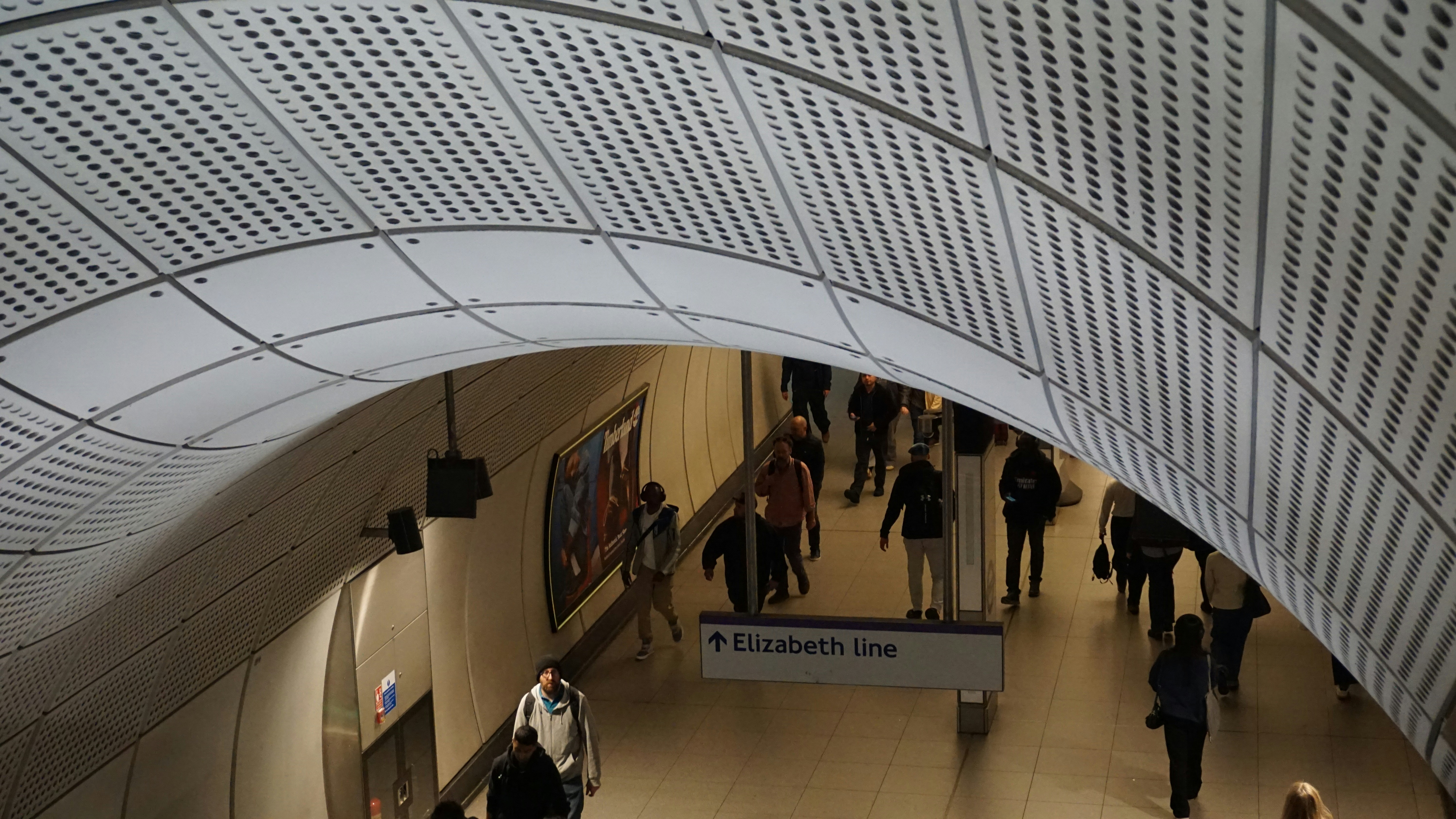 Passengers move through a modern underground station, elizabeth line visible.