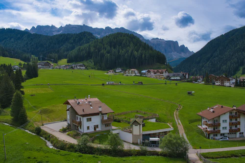 Prairie de fond de vallée et maisons à balcons de bois, forêt de conifères et sommets rocheux au fond