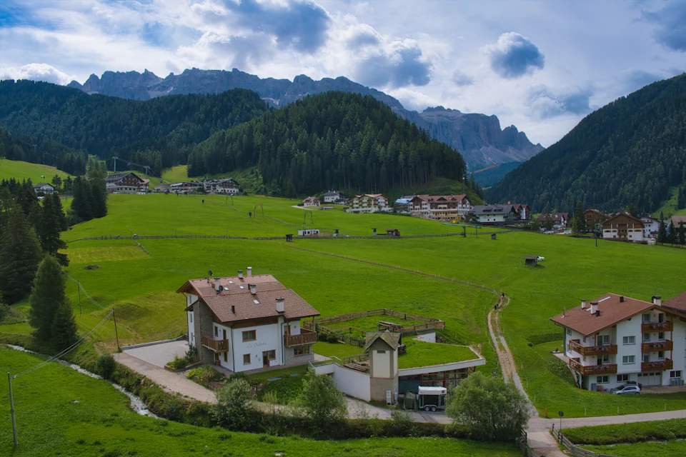 Prairie de fond de vallée et maisons à balcons de bois, forêt de conifères et sommets rocheux au fond