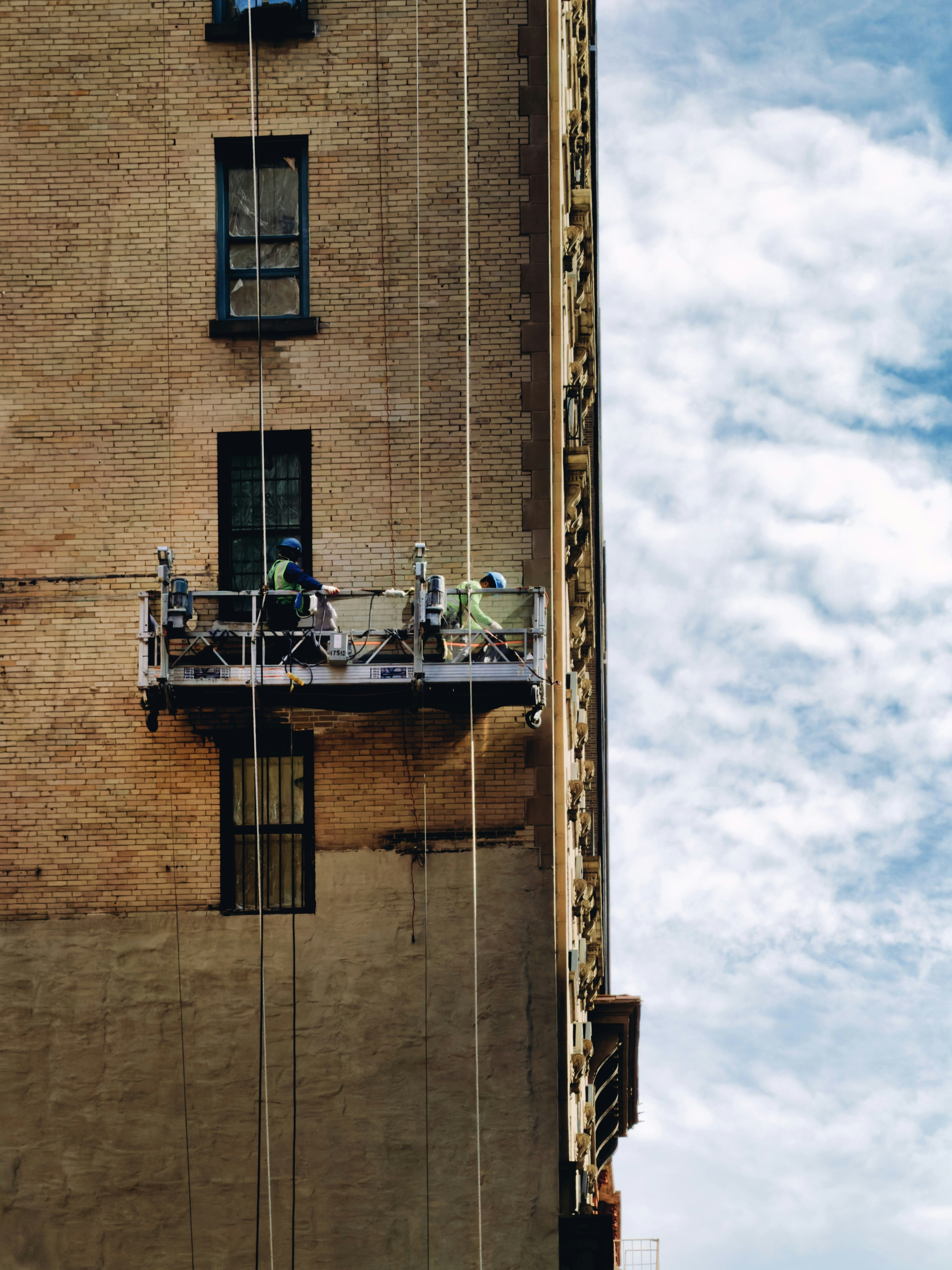 Workers on a suspended scaffold repairing a building facade.