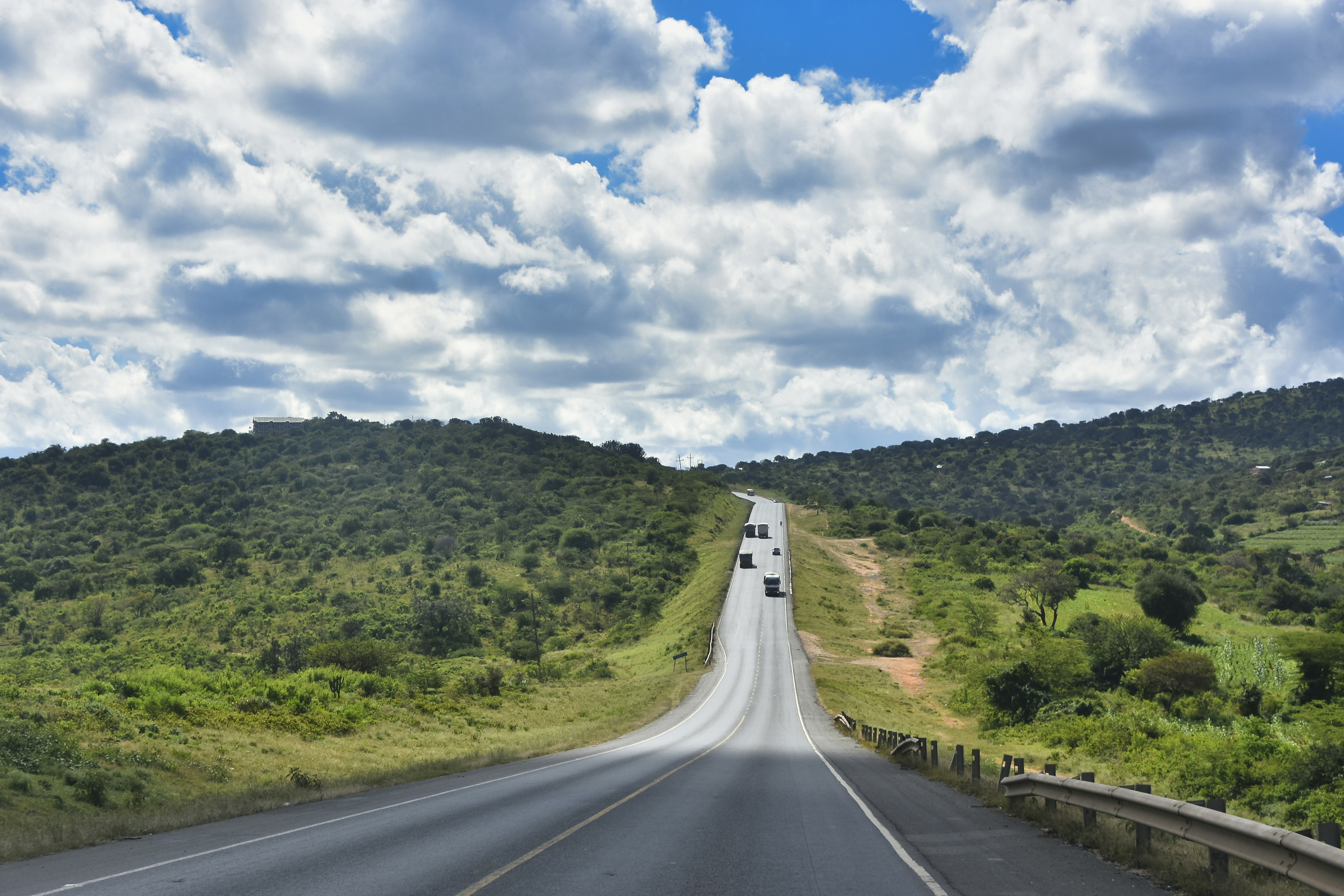 Road winding through green hills under a bright, cloudy sky.