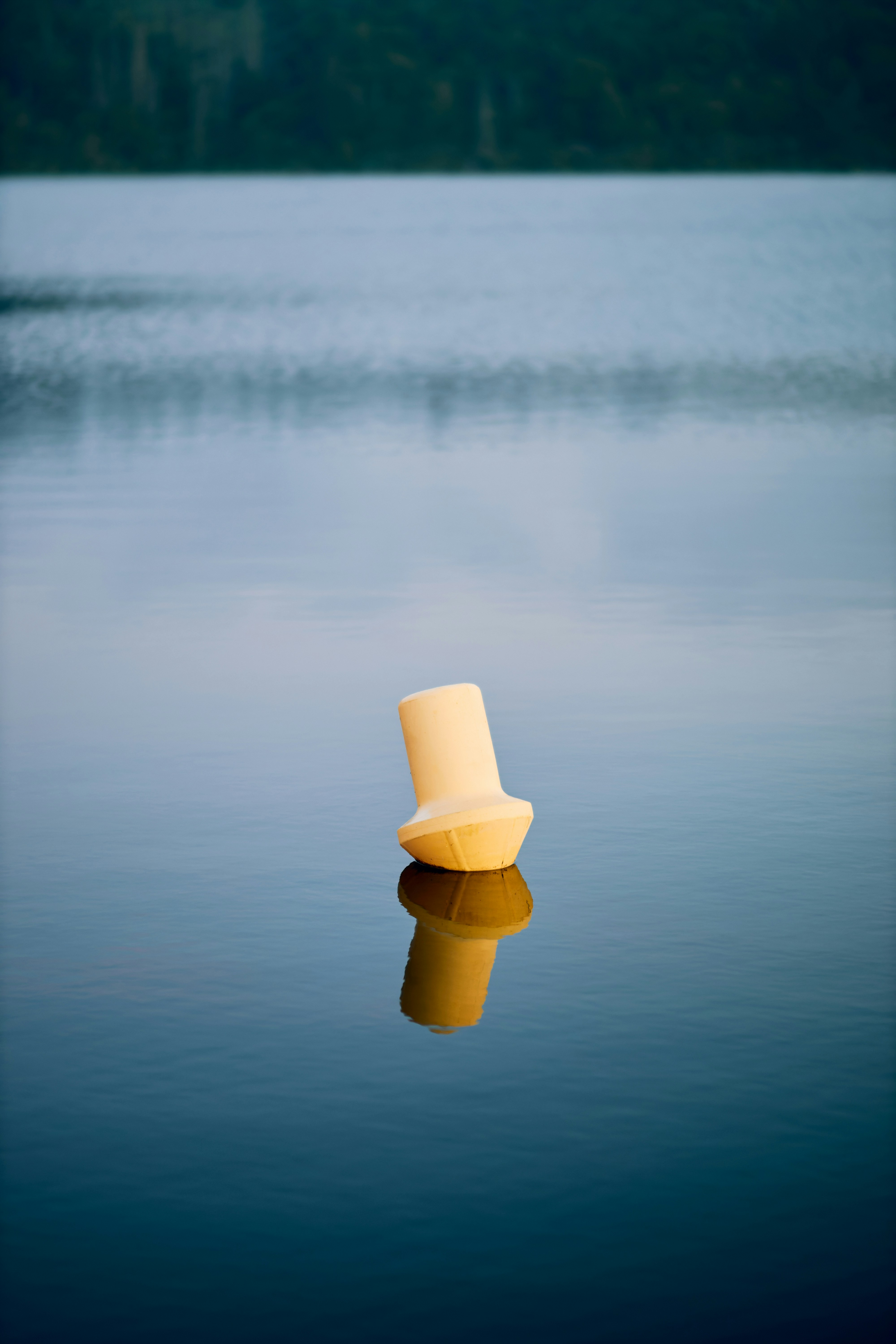 Yellow buoy reflecting on calm, blue lake water.