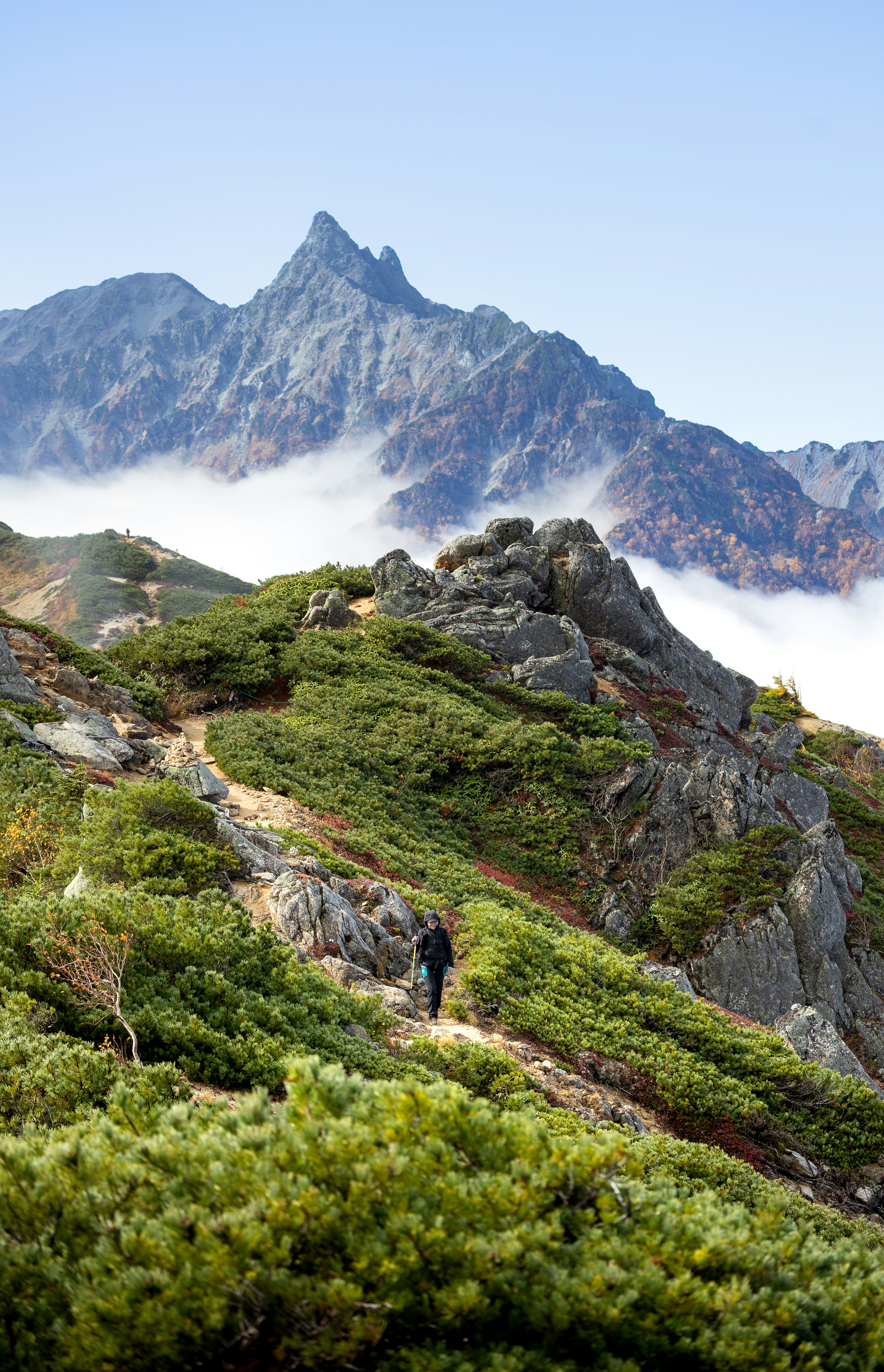Hiker ascends a rocky mountain path towards distant peaks.