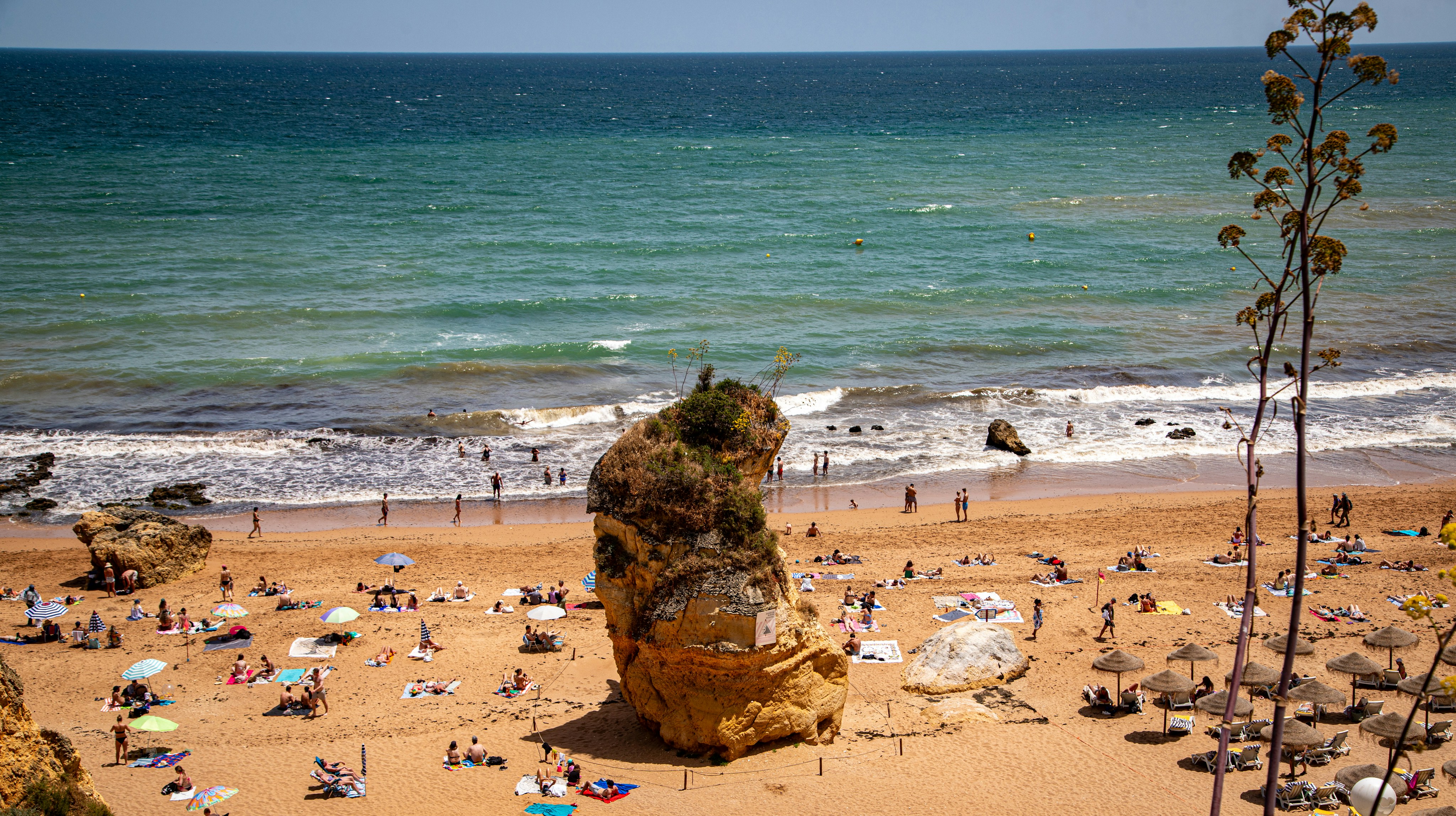 People relax on a sunny beach with a large rock.