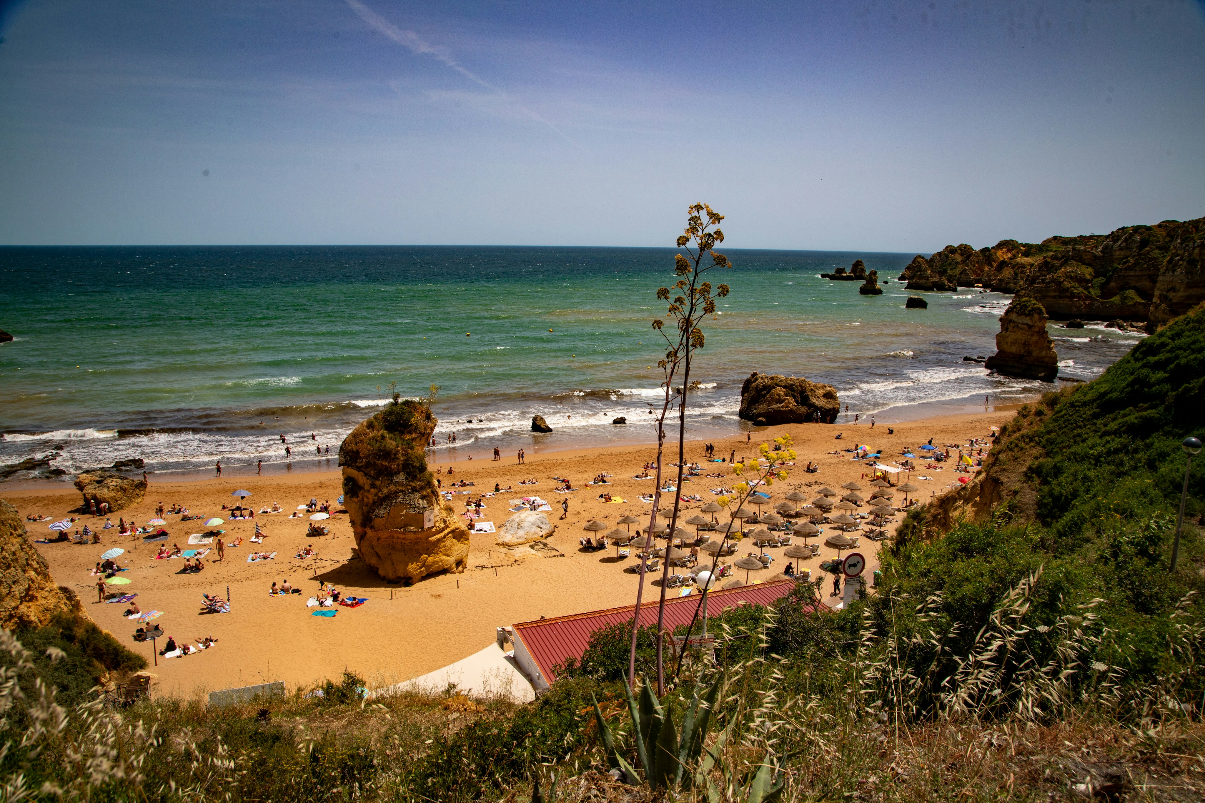 Coastal beach with people, umbrellas, and prominent rock formations.