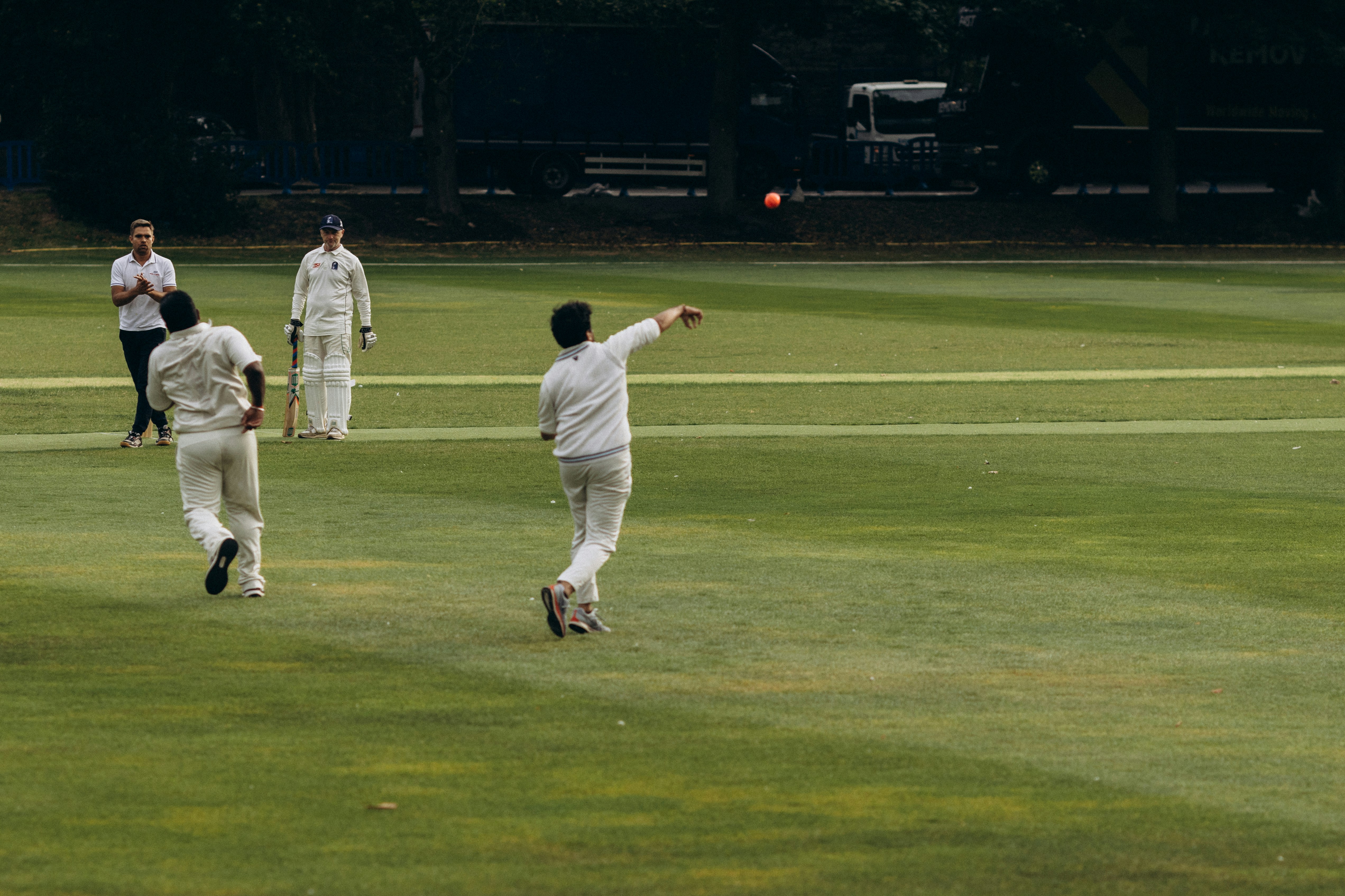 Cricketers on a green field, one bowling a red ball.