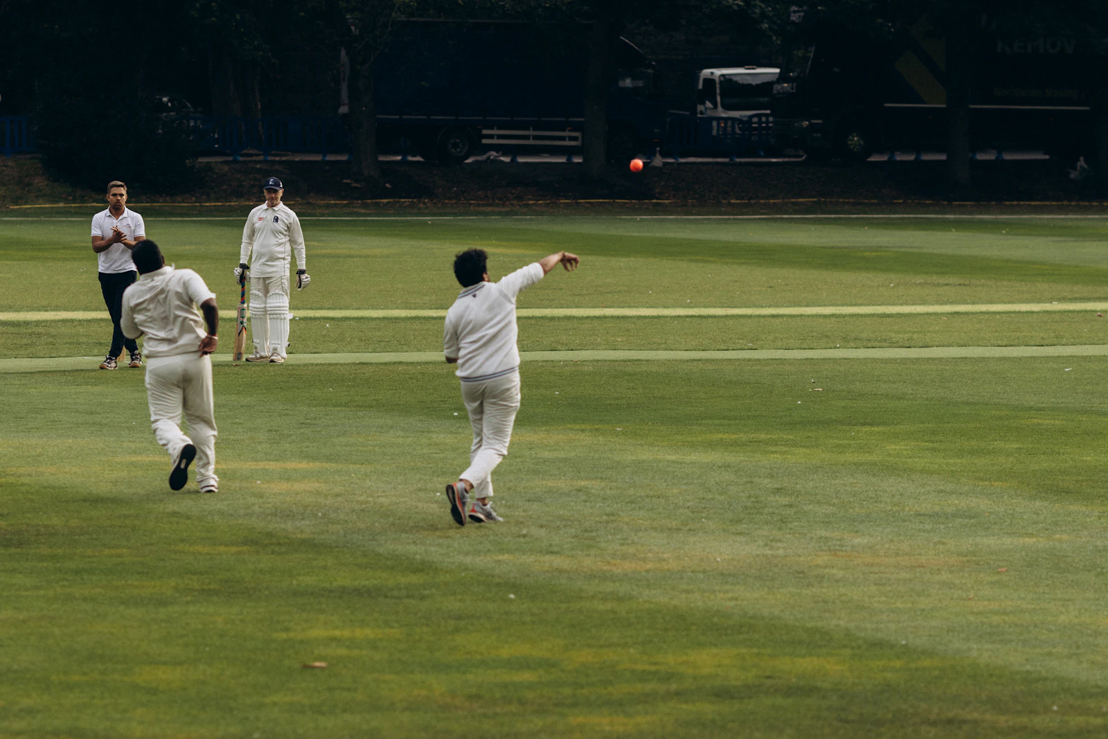Cricketer bowling a red ball on a green field