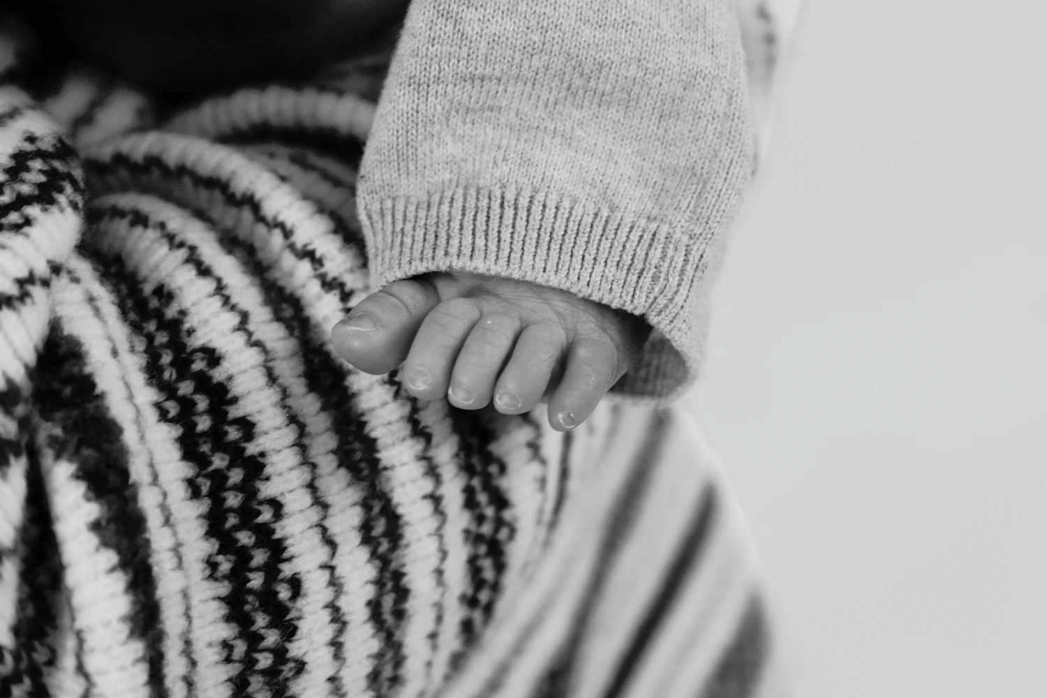 A child’s hand in a knitted sleeve resting on a striped blanket