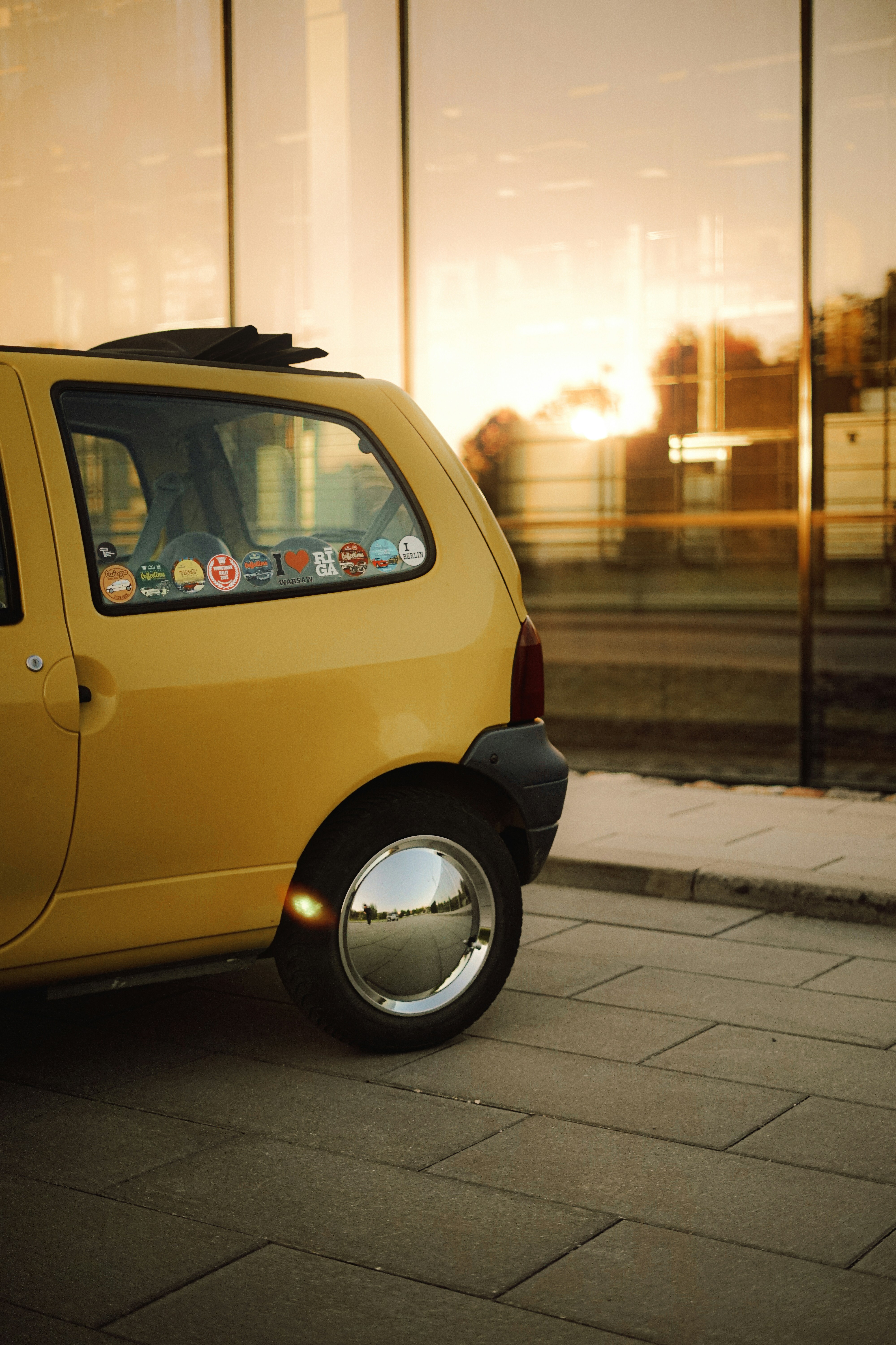 Yellow car parked beside a glass building at sunset.