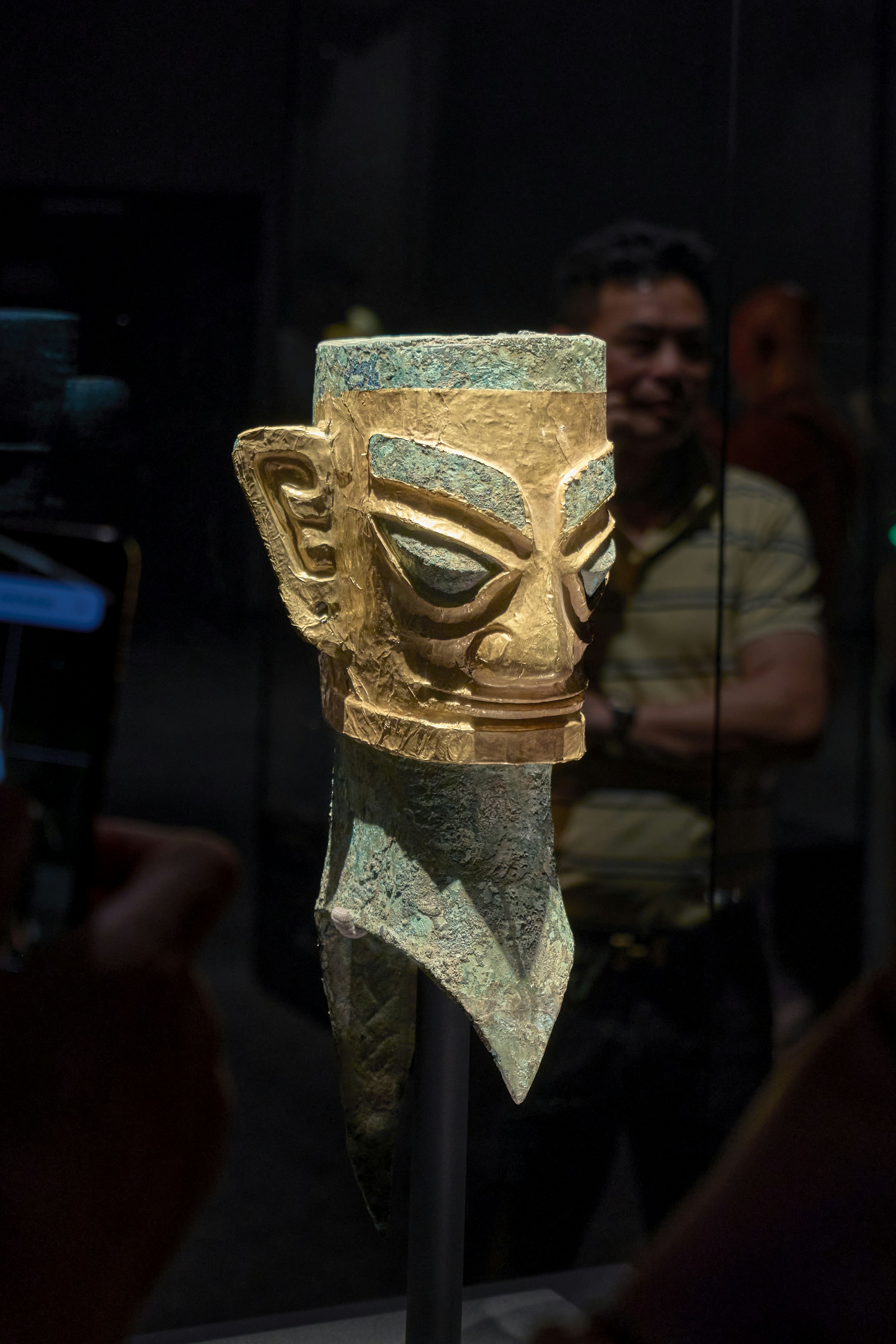 Artefato antigo de máscara de ouro e bronze sobre fundo escuro.