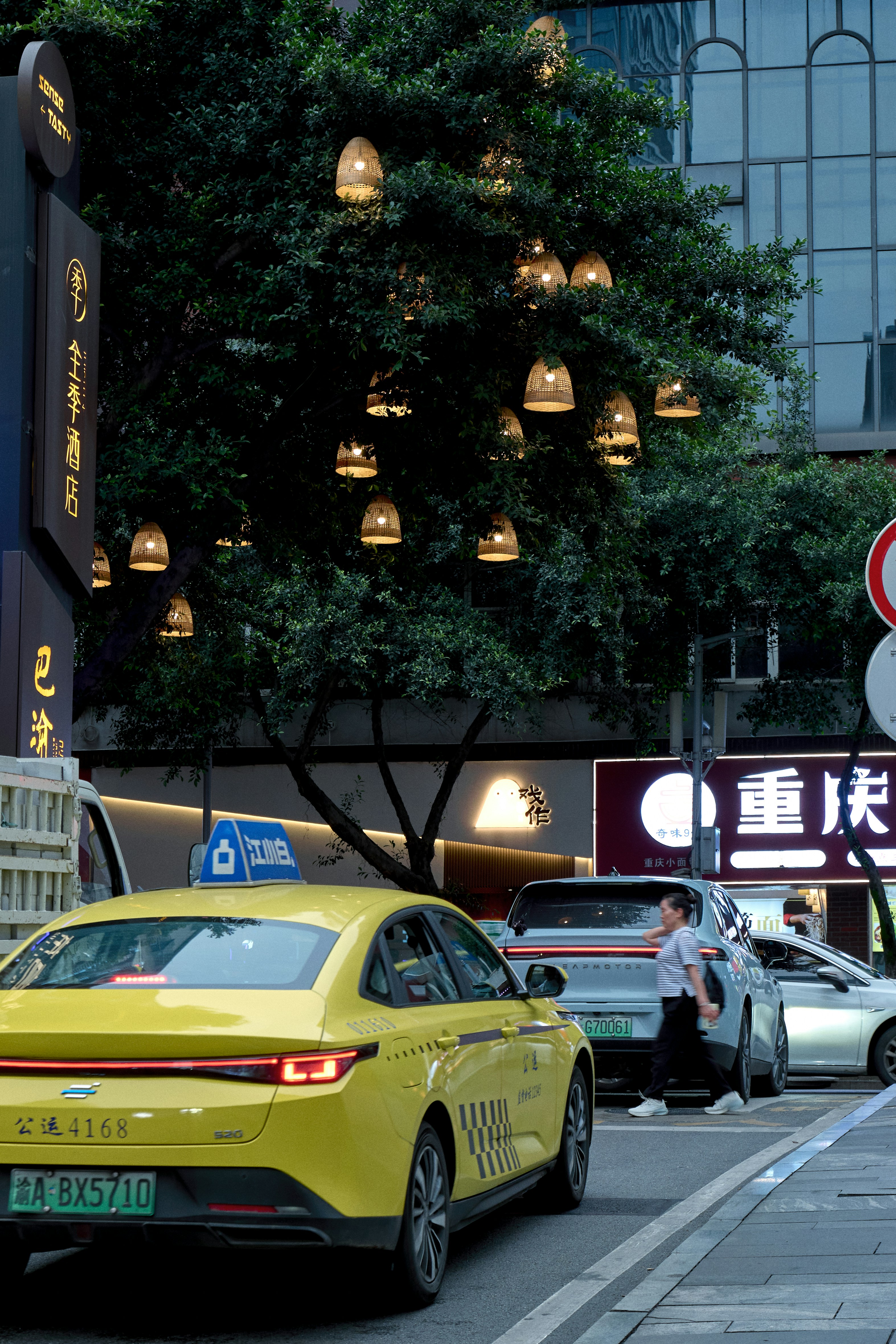 Táxi amarelo numa rua urbana com uma árvore iluminada por lanternas.
